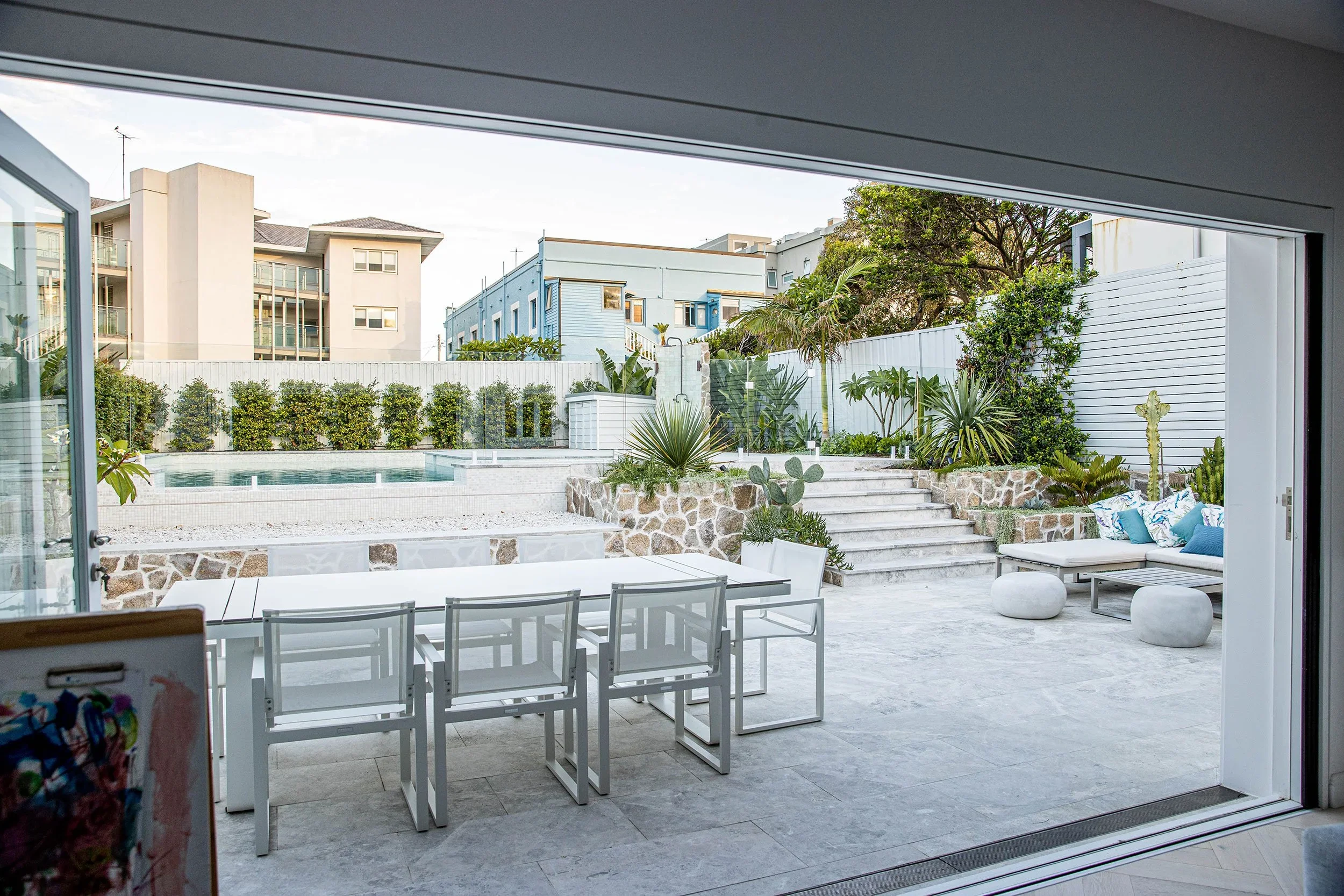 Patio and pool area viewed through open sliding doors with outdoor dining and landscaping.