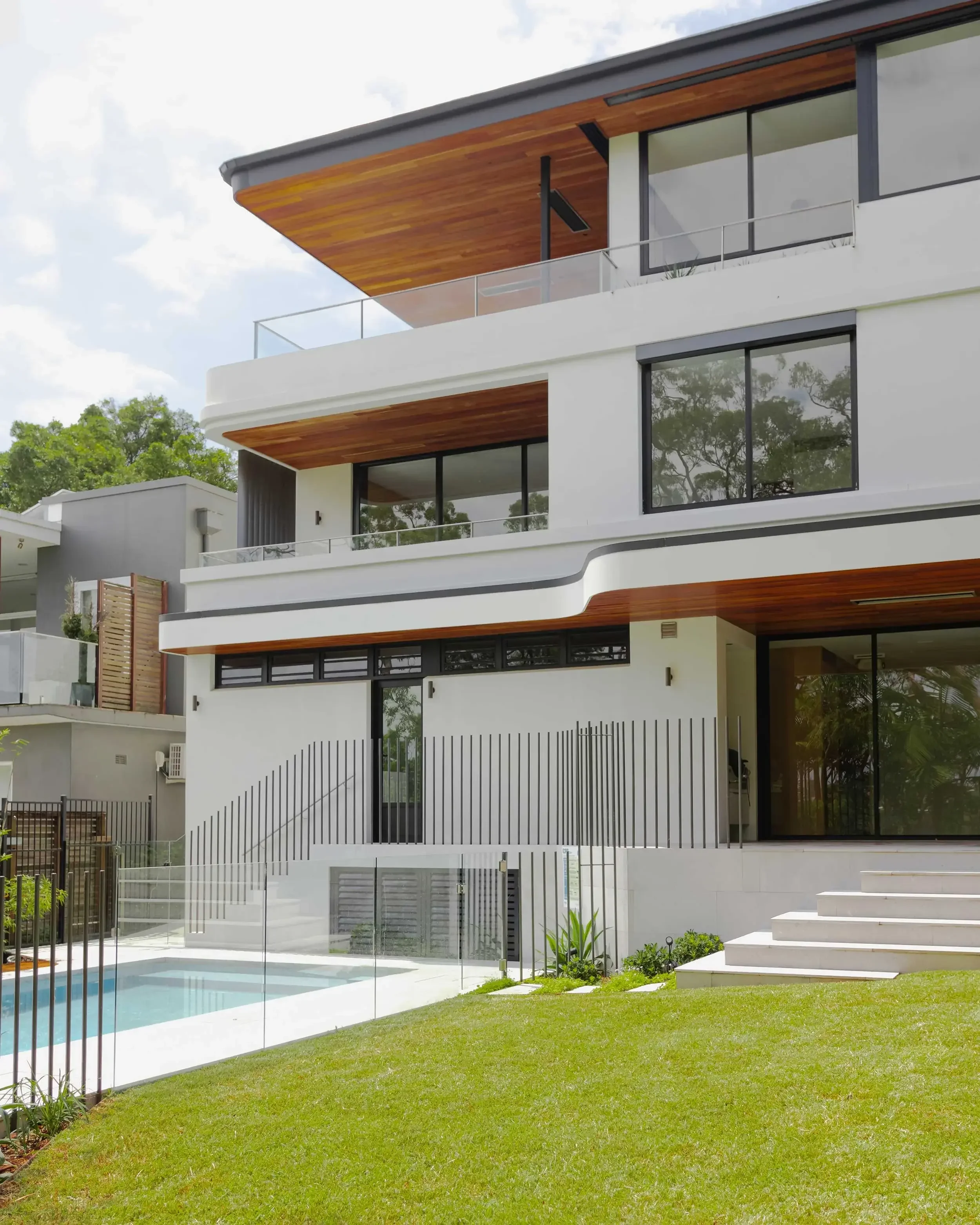 Modern multi‑story house exterior with wood‑accented balconies, large windows and a lawn