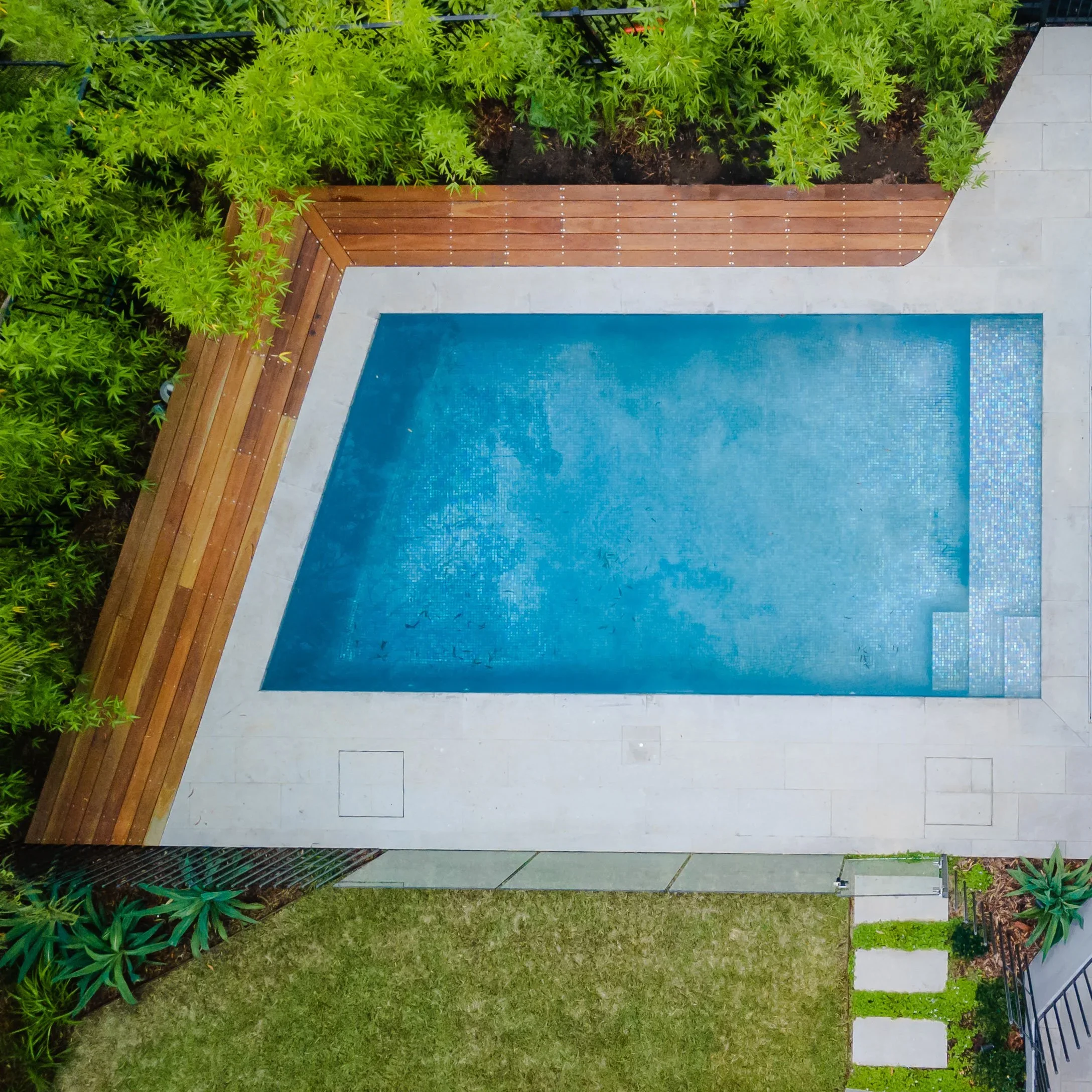 Aerial view of a blue pool with stone deck and surrounding greenery.