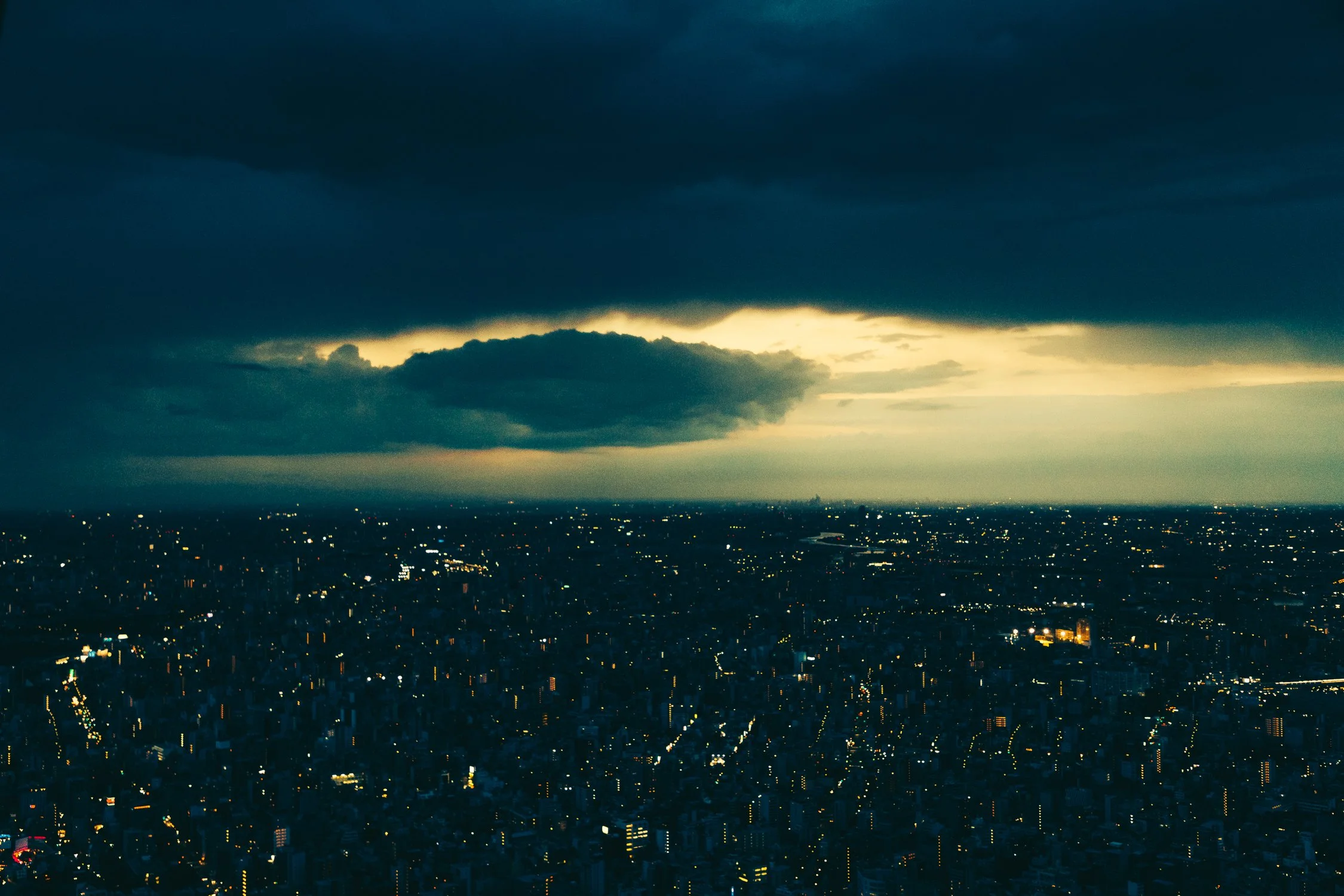 City skyline at night with illuminated buildings and dark storm clouds overhead, with a break of light near the horizon.