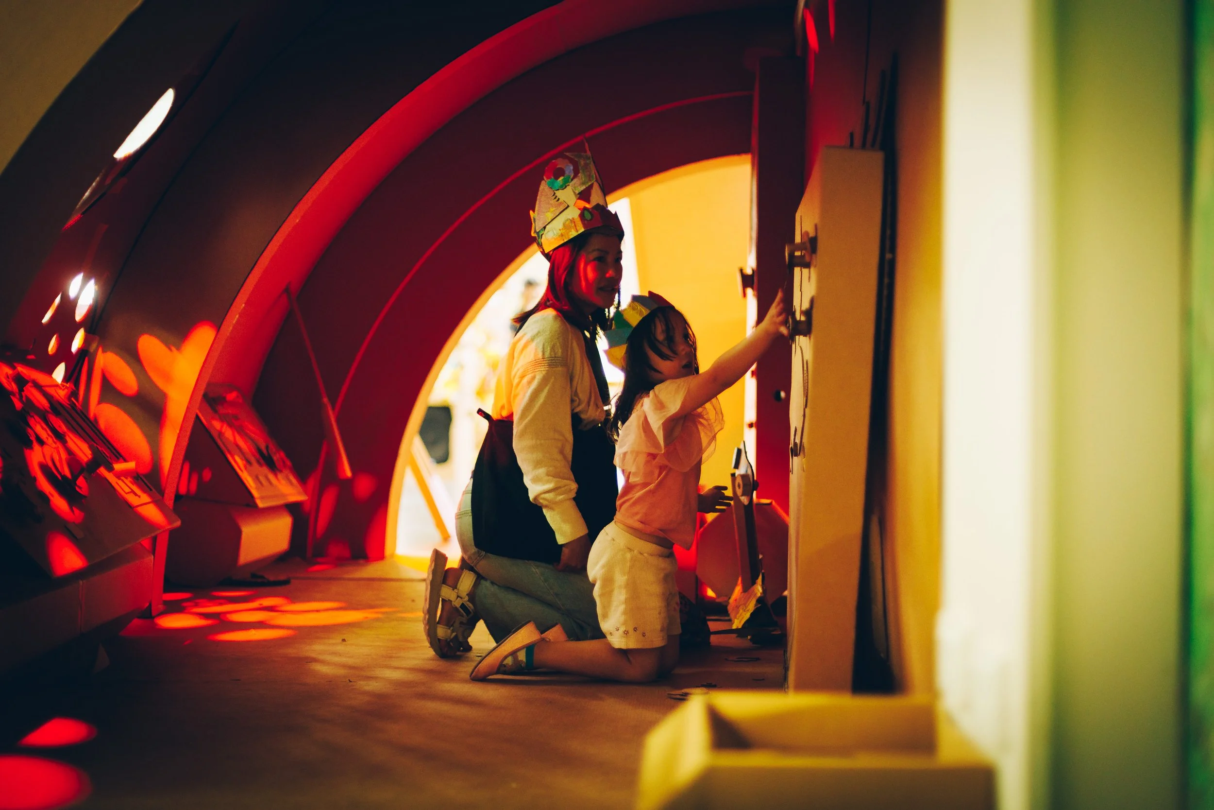 A woman and a young girl kneeling and interacting with an exhibit in a museum with blue and yellow lighting.