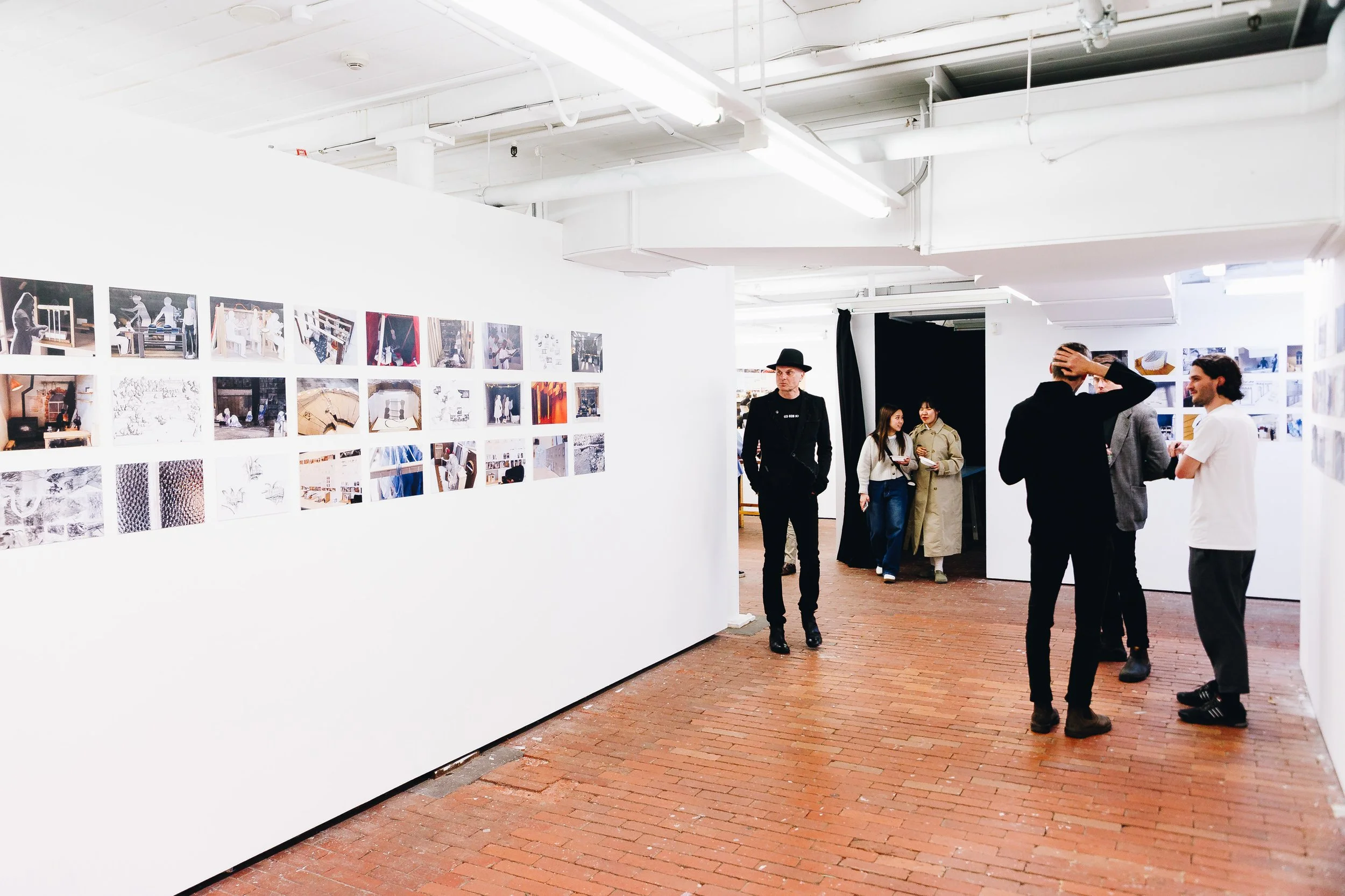 People viewing artwork and photographs in an art gallery with white walls and brick floors.