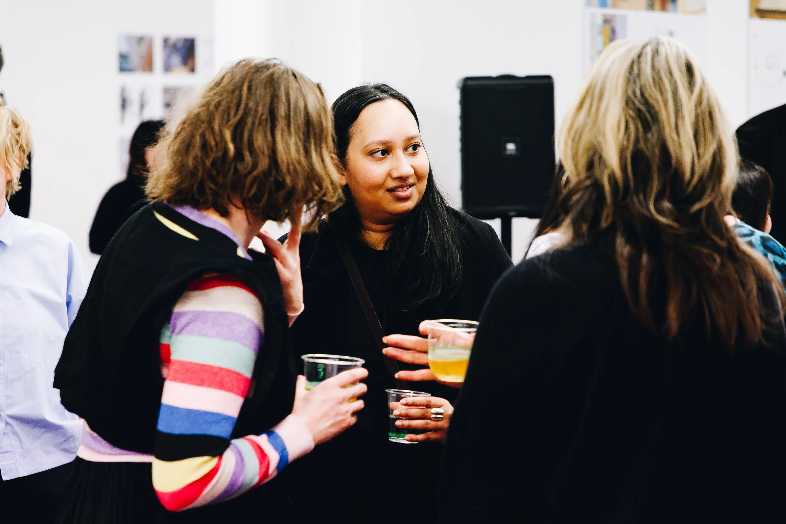 Group of women talking at a social event, holding drinks, in an indoor setting.