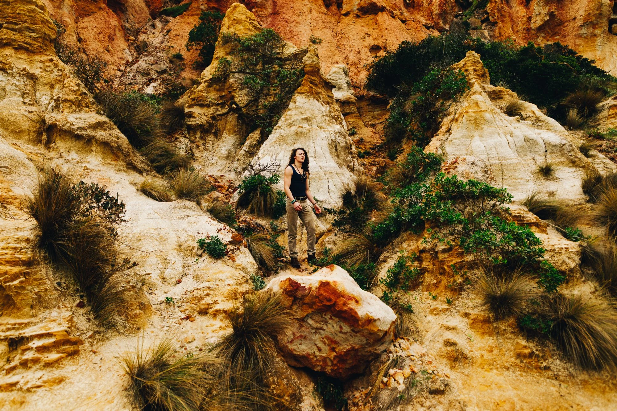 A woman standing on a rock in a desert landscape with rugged cliffs and sparse vegetation.