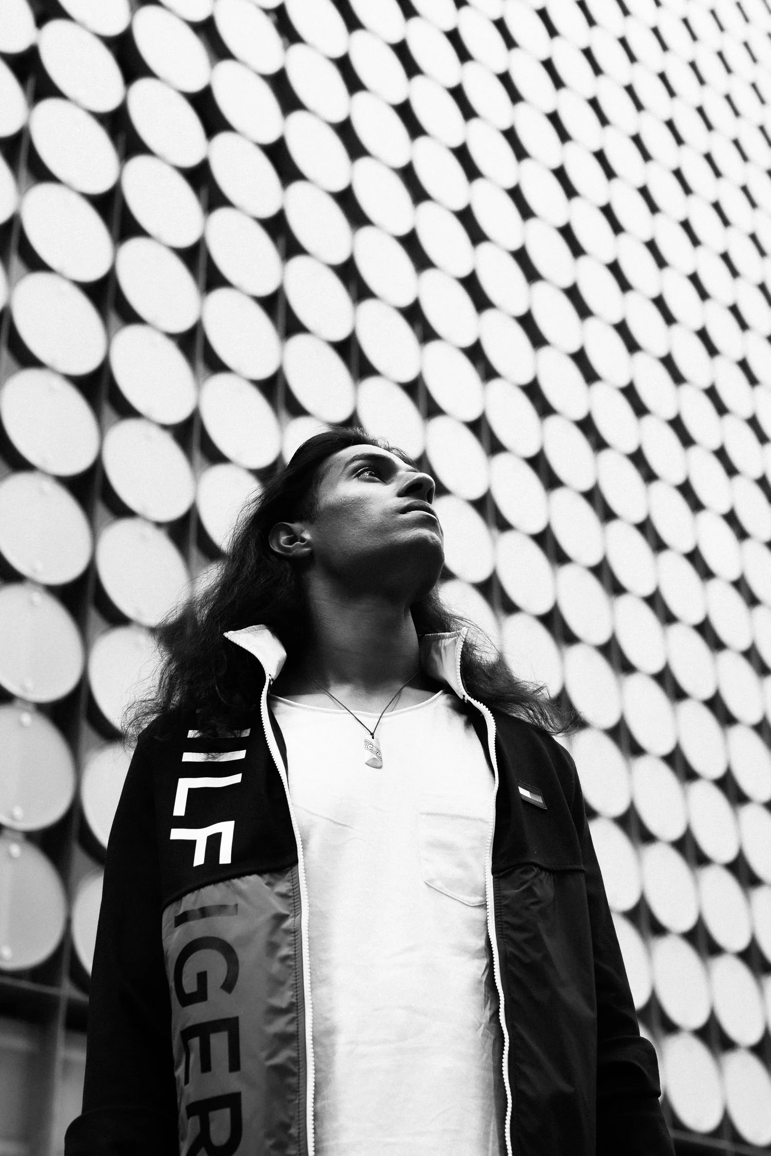 A person with long hair looking up, standing in front of a wall made of circular panels.