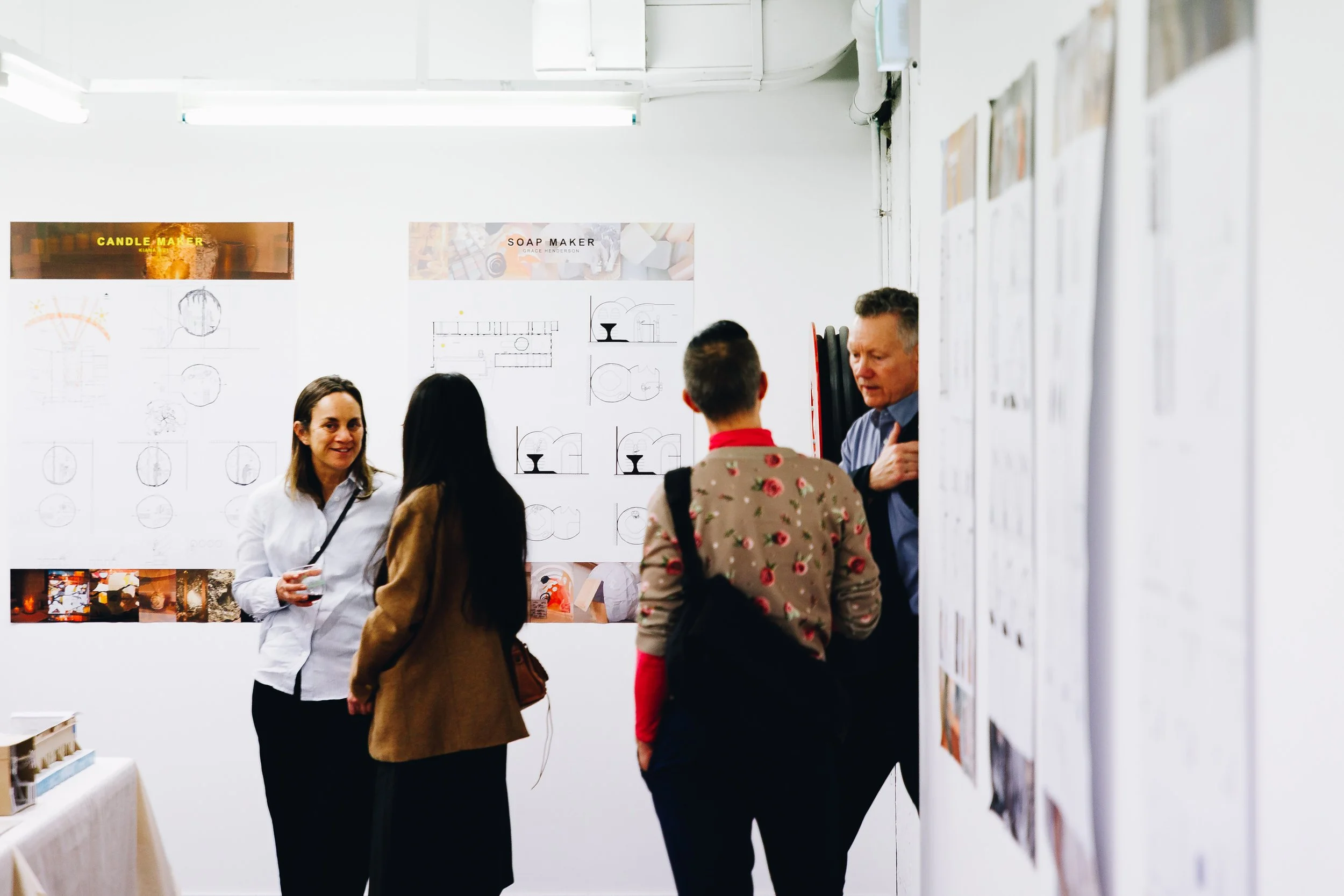 People talking at an event with design layout boards on the wall.