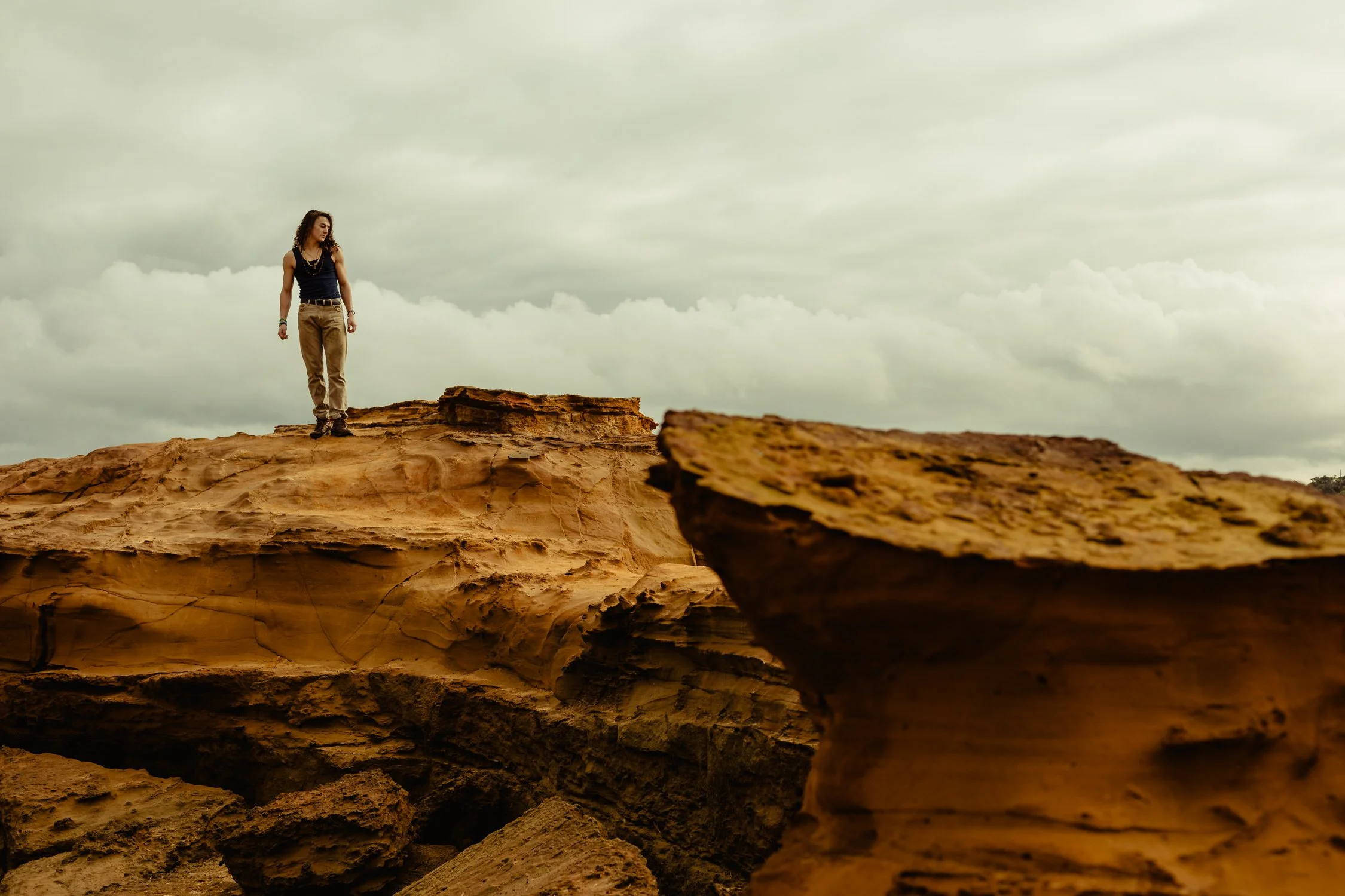 A woman standing on a rock formation in a desert landscape with cloudy skies above.