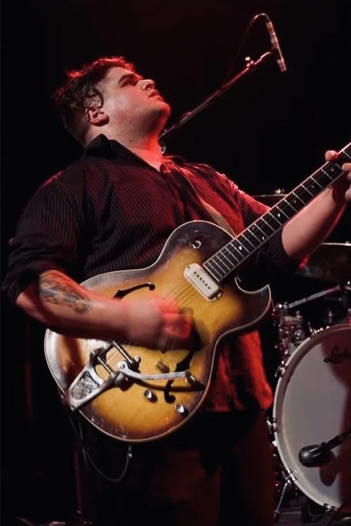 Musician playing an electric guitar on stage during a performance.