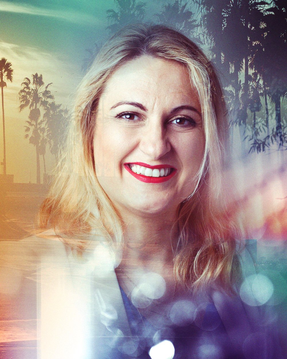 A young woman with long brown hair smiling, standing in front of a window with a city skyline reflecting over her. The photo has a double exposure effect combining her portrait and the cityscape.