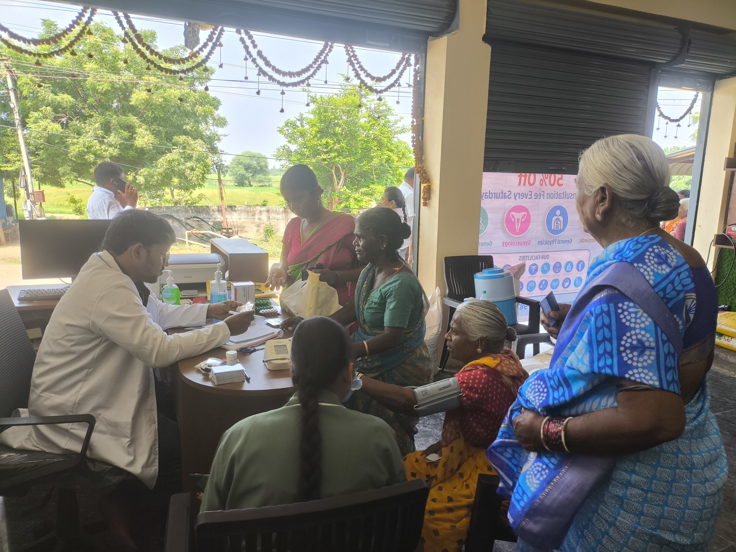 Farmers attending a health awareness session in a room decorated with hanging garlands, with a woman addressing the group and health information displayed nearby.