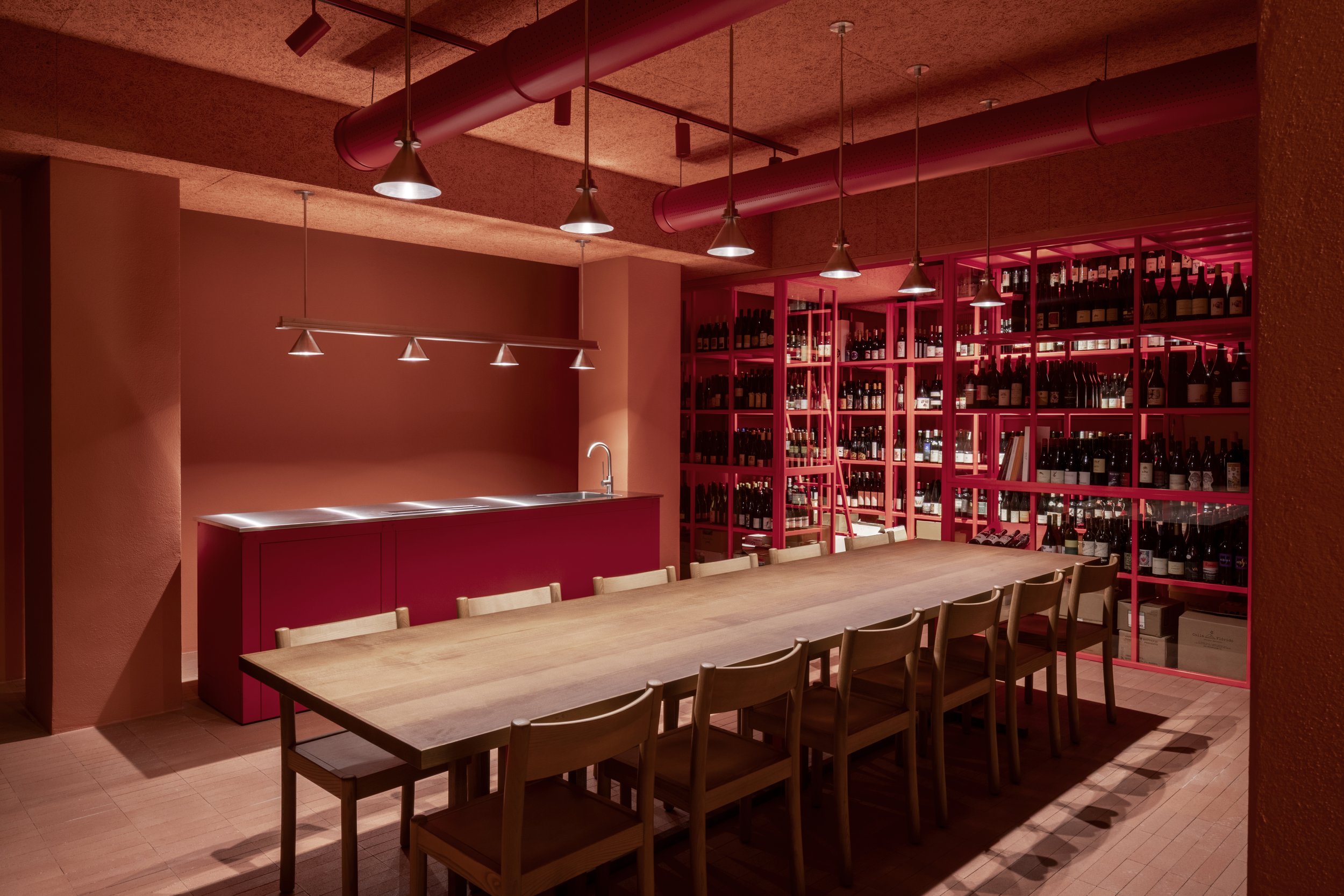 a long wooden table with chairs and a bar with wine bottles