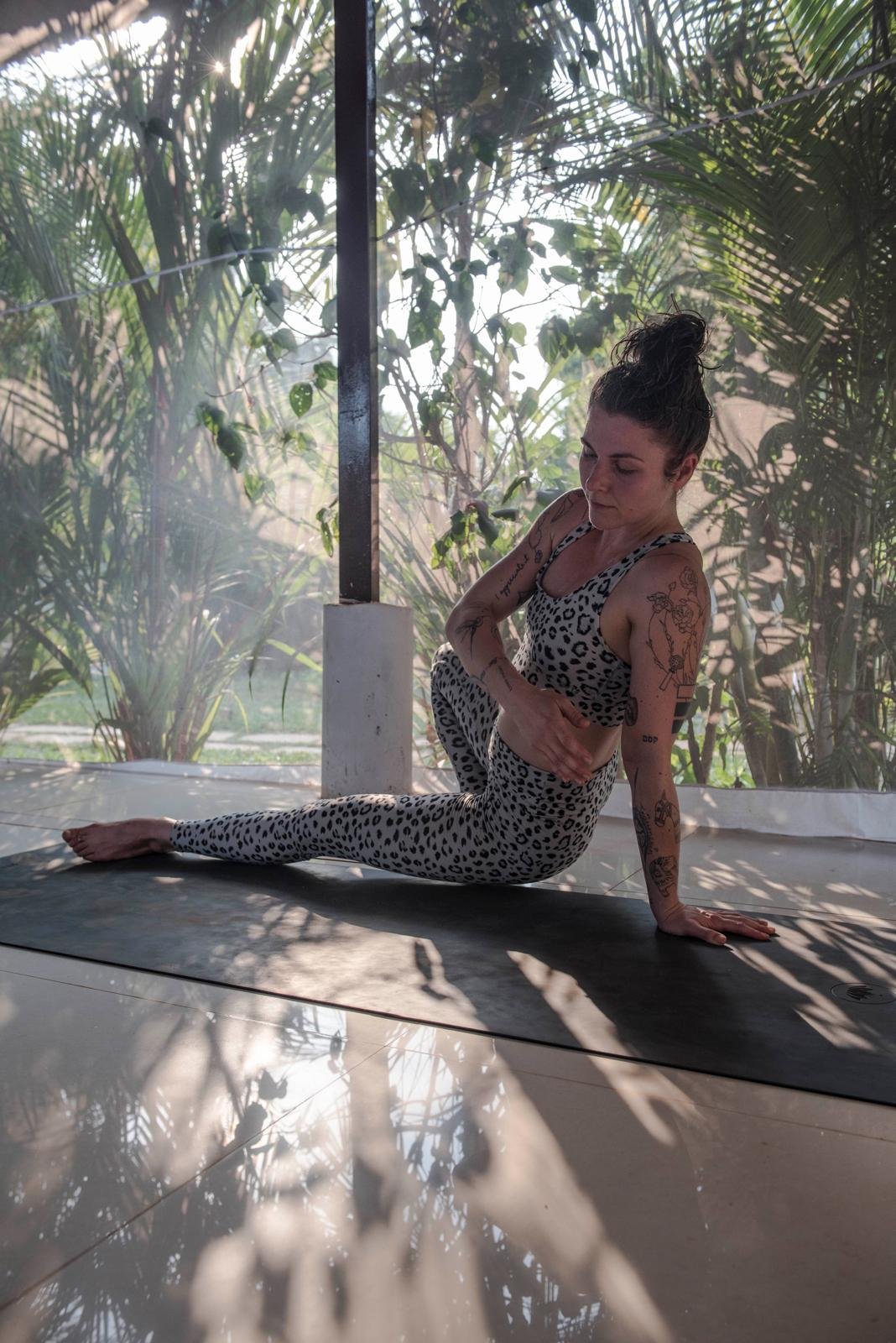 Person practicing yoga indoors in a leopard-print outfit, surrounded by plants, with sunlight streaming in.