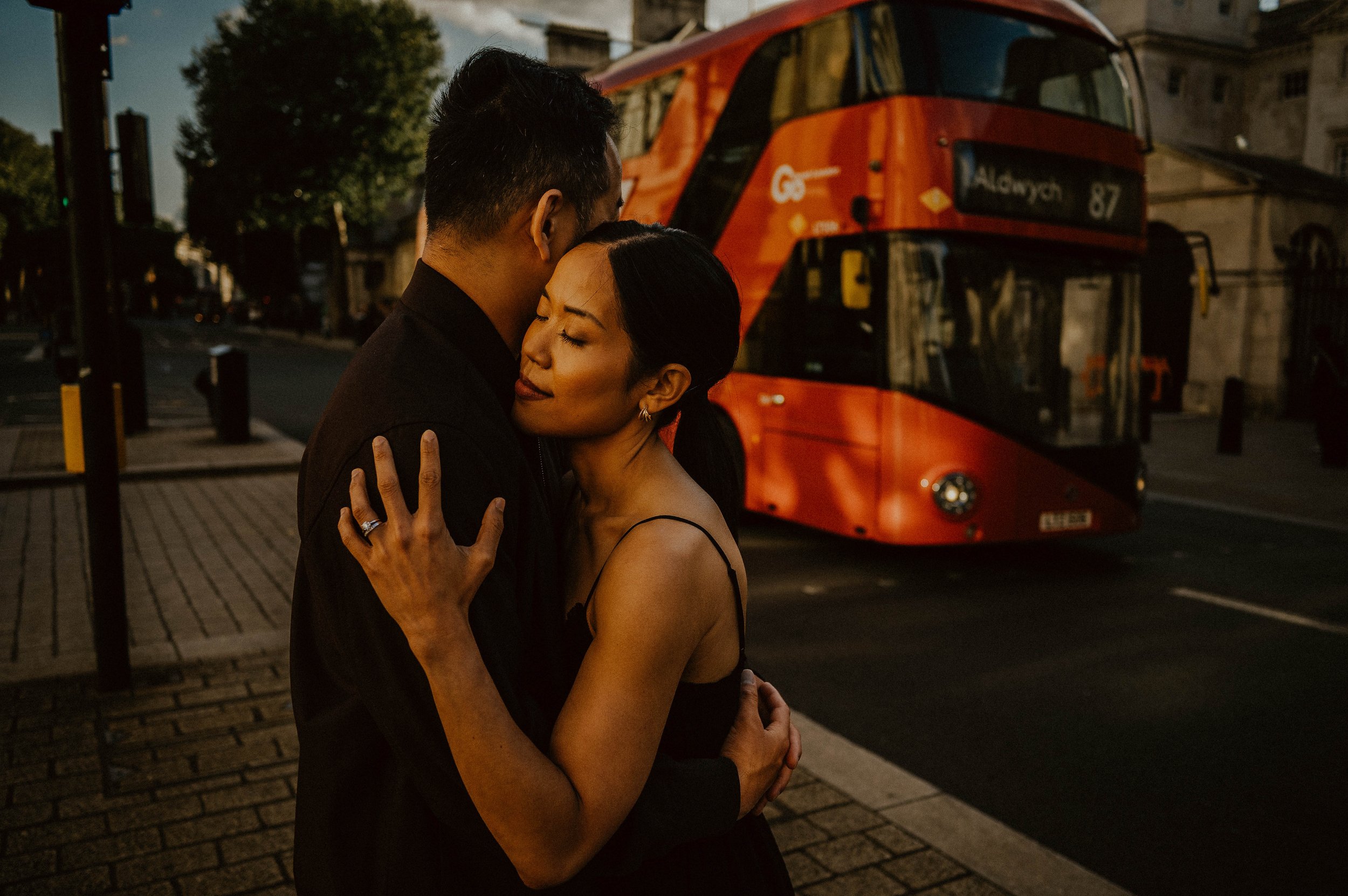 A couple hugging on a city street at dusk, with a red streetcar in the background.