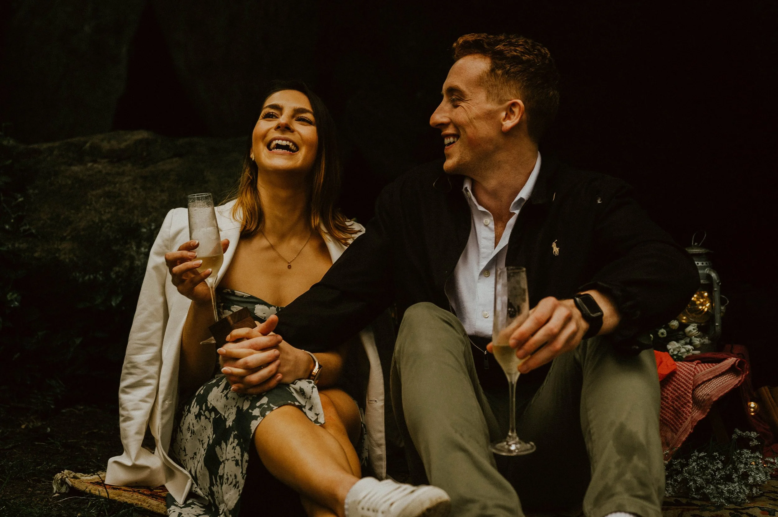 An heterossexual couple having a picnic in the woods and drinking champagne while laughing and gazing at each other