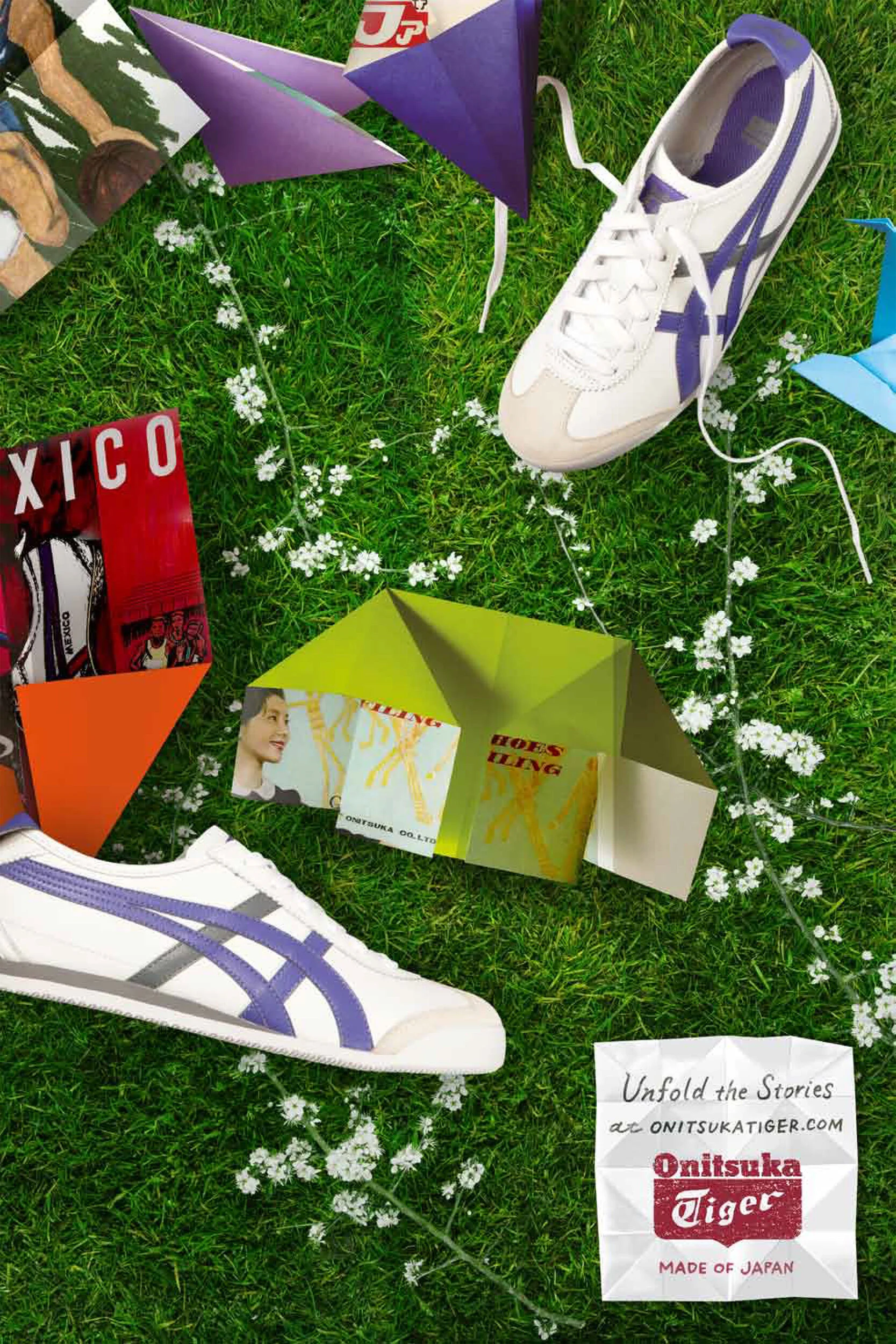 Green grass with small white flowers scattered across, featuring white and purple sneakers, colorful pamphlets, origami paper boats, and a white paper sign with black and red text promoting Onitsuka Tiger shoes.