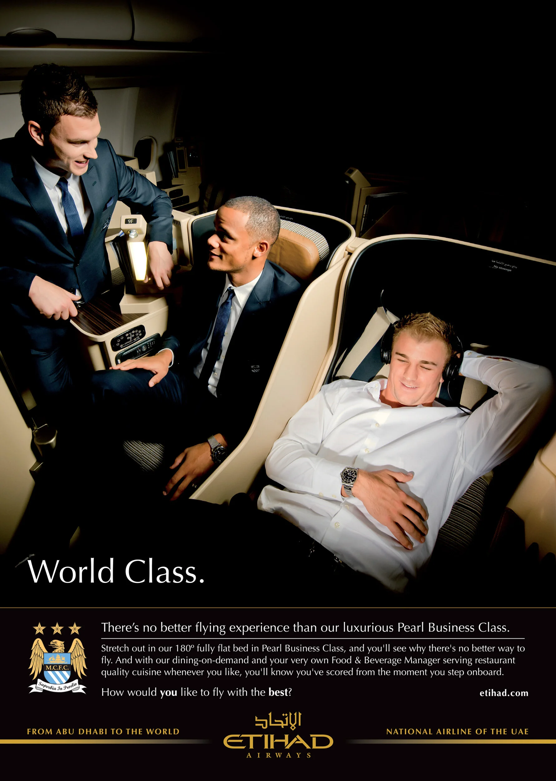Two men in business attire are sitting and standing inside a luxurious airplane. One man is sitting with his eyes closed, wearing headphones, and the other man is standing, leaning on the seat, engaging in conversation.
