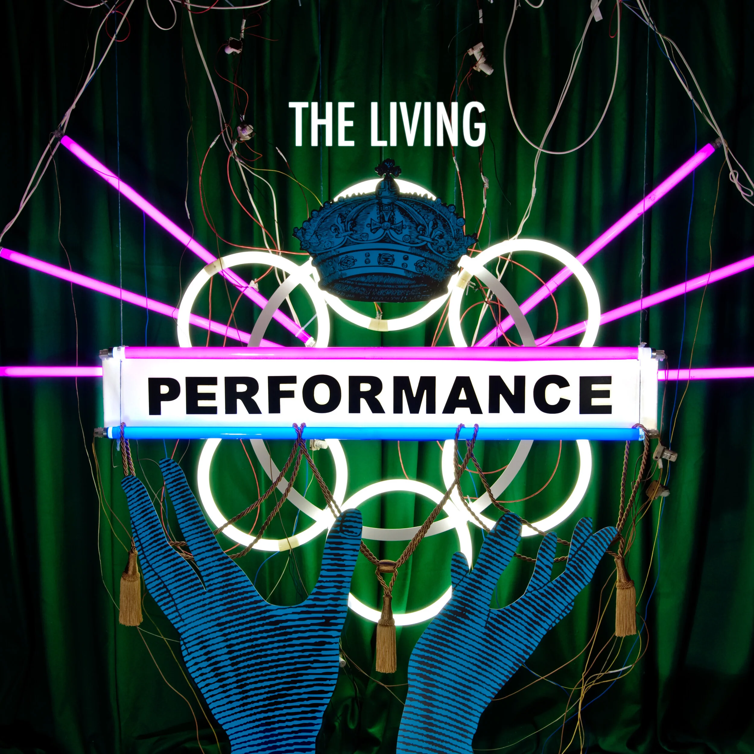 Neon sign reading 'The Living Performance' with a crown and two blue, striped hands making gesture in front, set against a dark green curtain with pink and white neon lights.