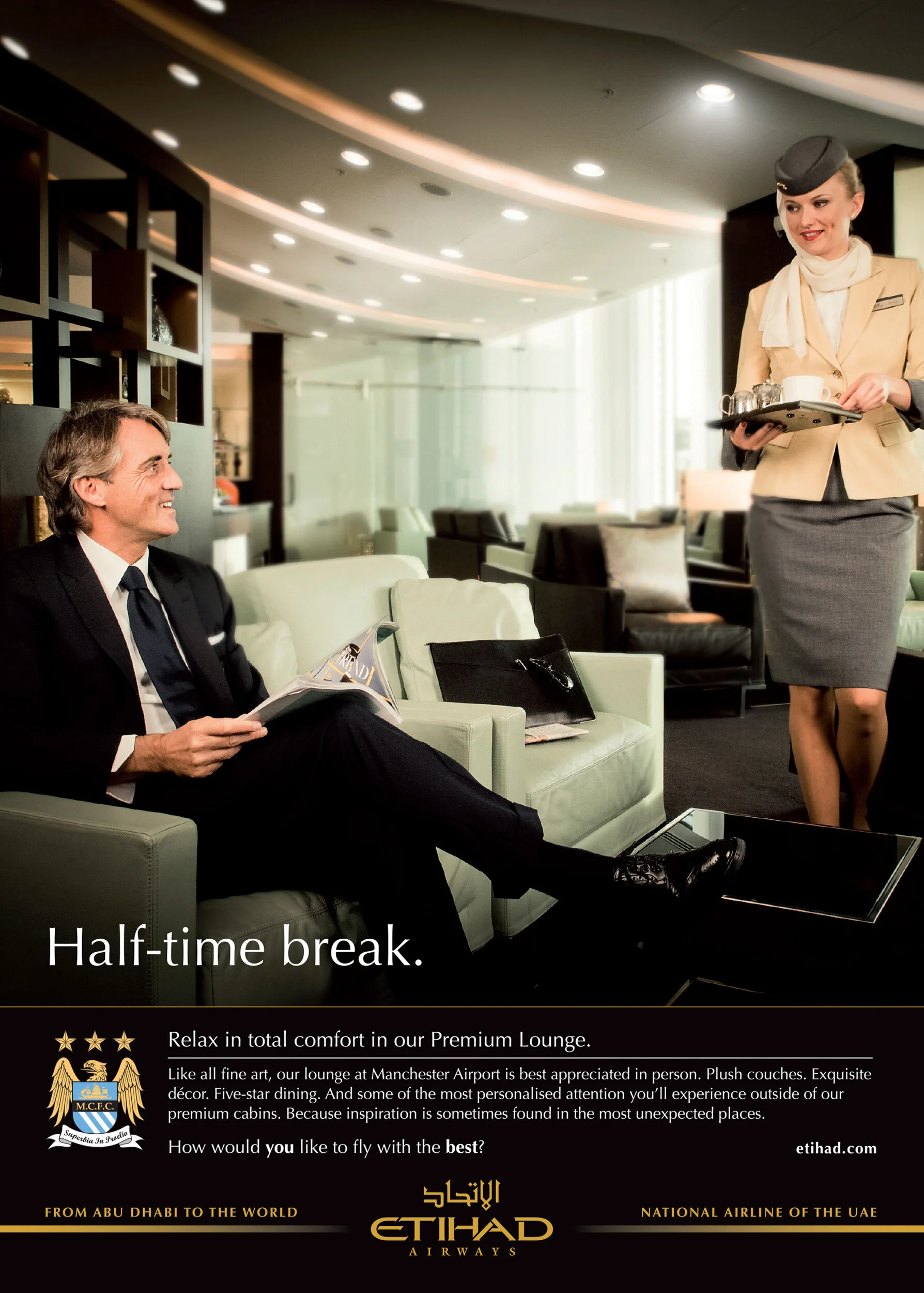 Man in business suit sitting on sofa, reading a magazine, with a woman in airline uniform serving drinks. The setting appears to be a luxurious airport lounge.