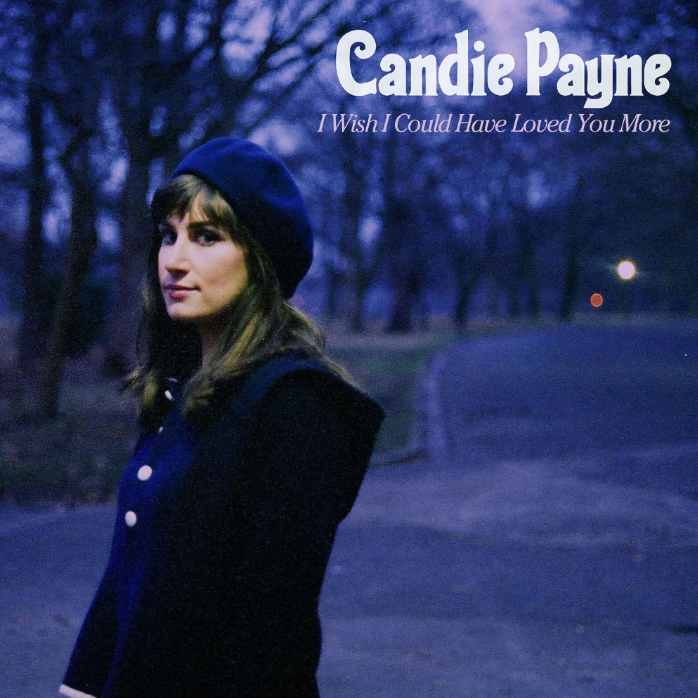 Album cover for Candie Payne's "I Wish I Could Have Loved You More" featuring a woman with brown hair wearing a blue beret and a dark coat outdoors at dusk, with a tree-lined path in the background.
