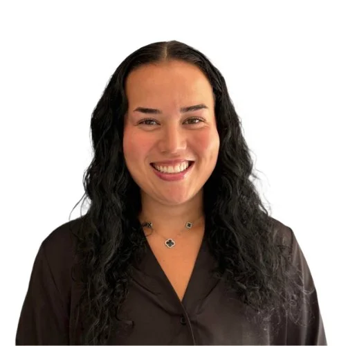 A woman with long, dark, wavy hair smiling at the camera against a plain white background.