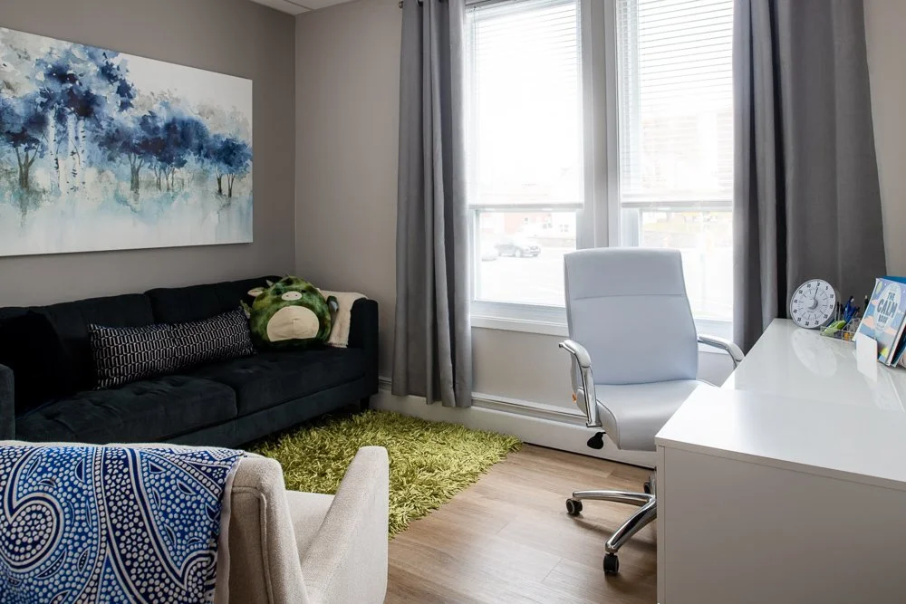 Counselling room at Spirit Psychological with cream chair, brown couch, green soft rug, abstract art on the wall, white desk and chair.