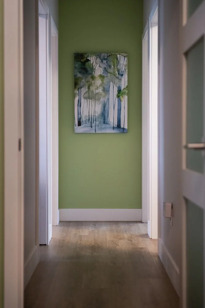 Hallway at Spirit Psychological with wood floor, green wall, and abstract art in green and blue