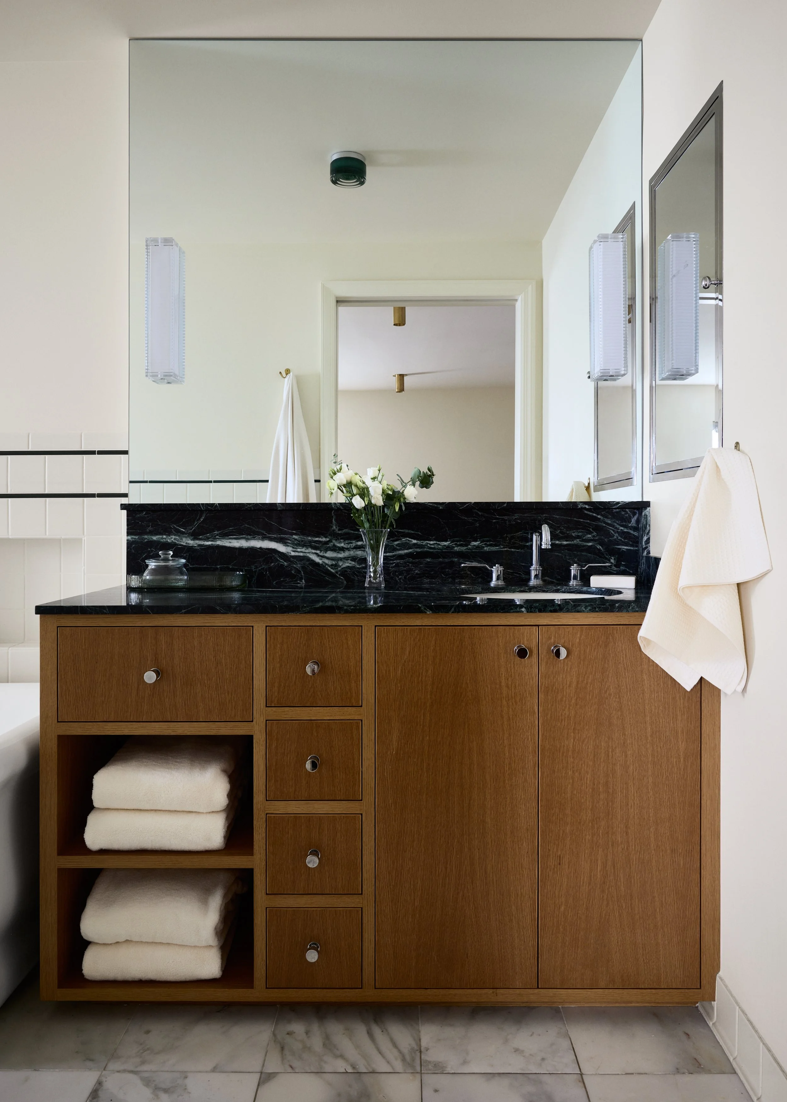 Bathroom vanity with a black marble countertop, a mirror, a flower vase, and a towel hanging on the right side.