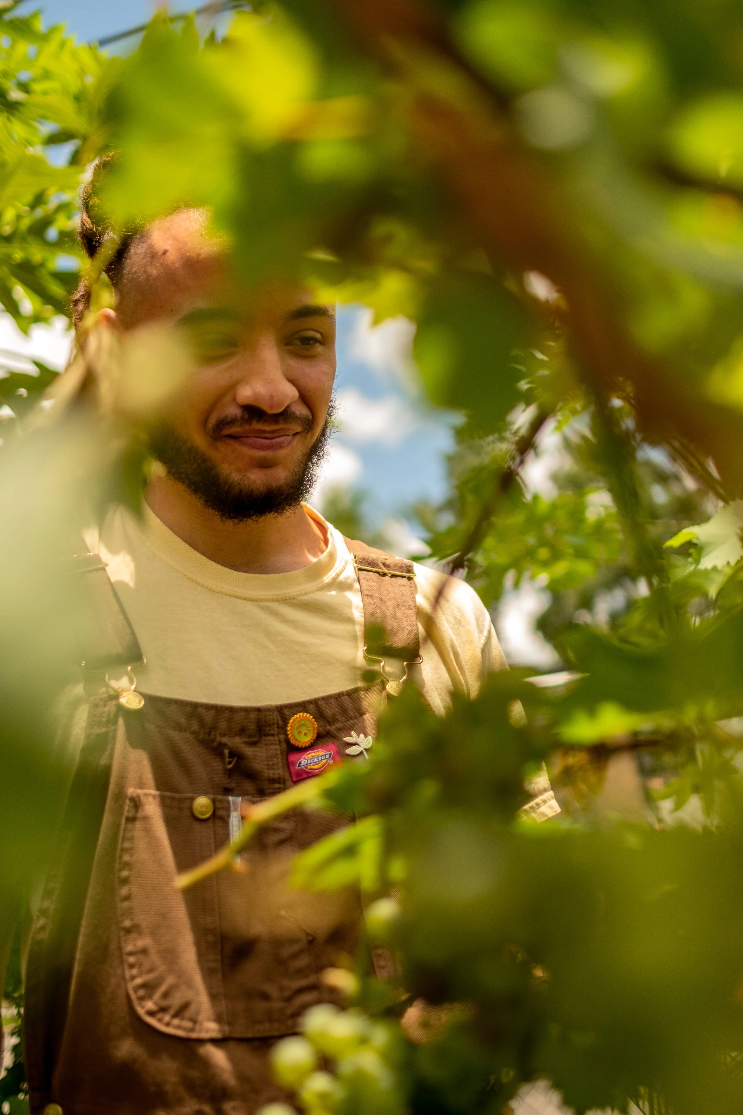 A smiling man in overalls peering through foliage