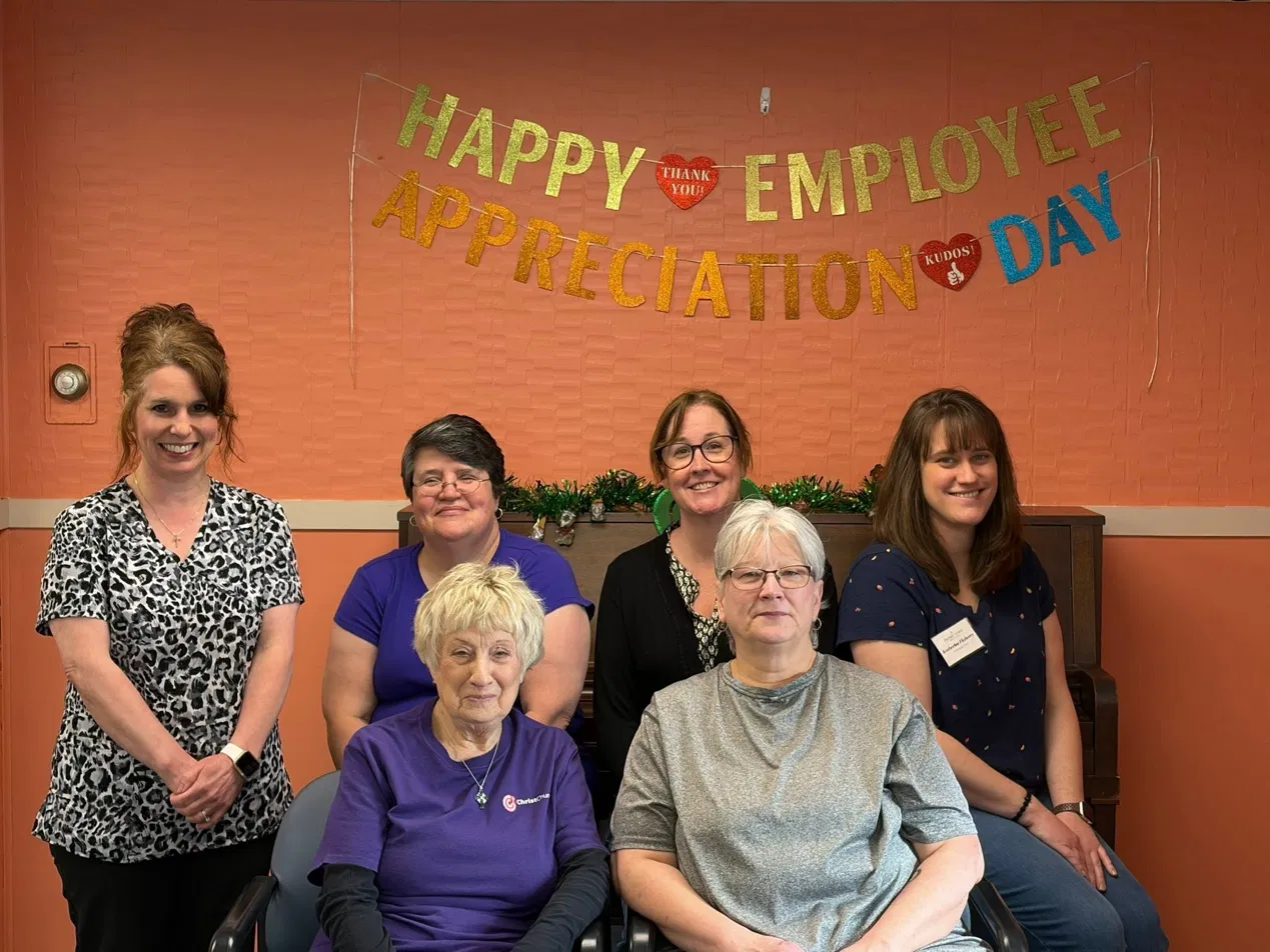 Group of six women gathered for Employee Appreciation Day celebration with a colorful banner in the background.