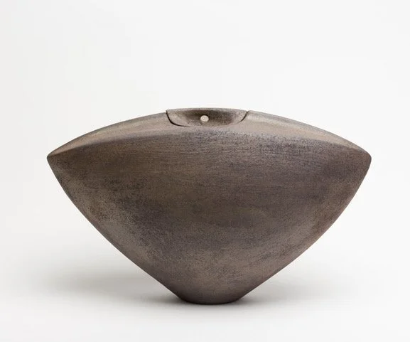 A softly triangular ceramic jar, with a small base and wider flared top. The jar is glazed with Wayne's "cast iron" glaze which is different mottled shades of brown.