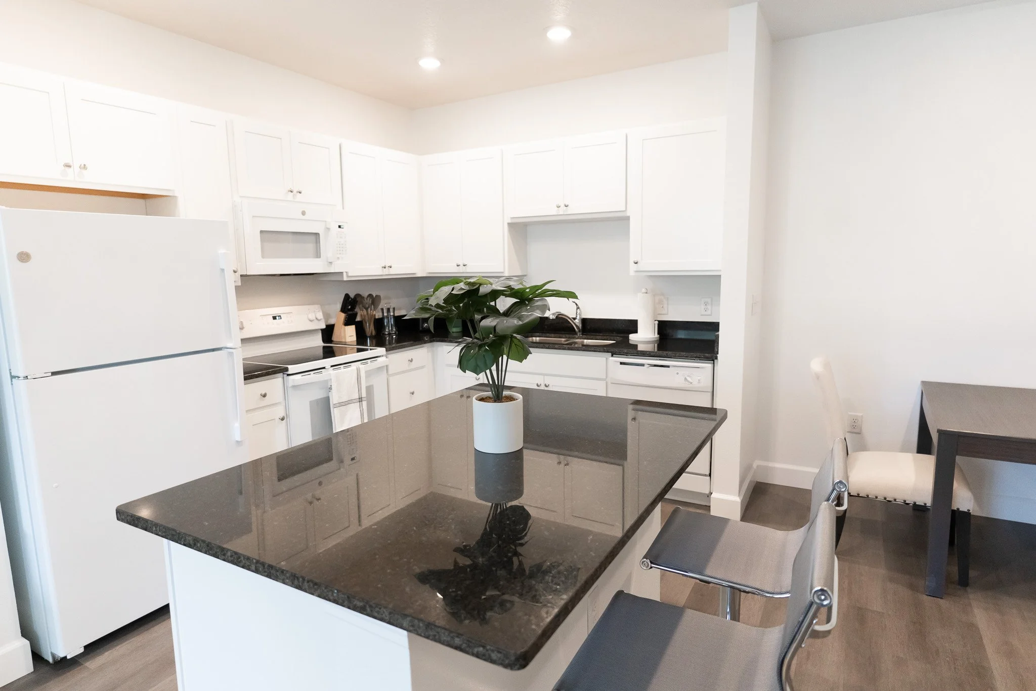 Modern kitchen with white cabinets, black countertops, white refrigerator, stove, microwave, and a potted plant on a black granite island.
