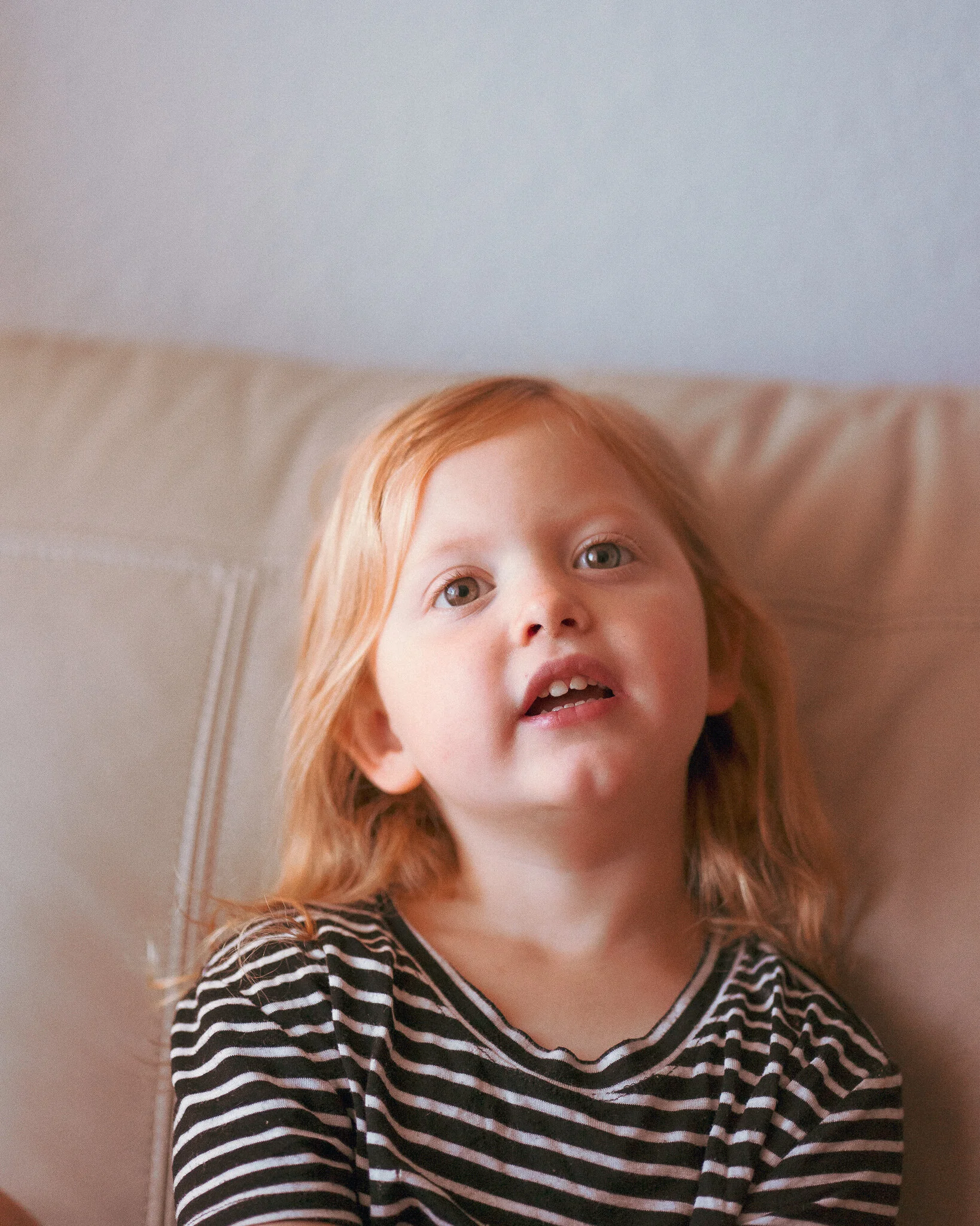 A young girl with red hair, wearing a black and white striped shirt, sitting on a beige couch.