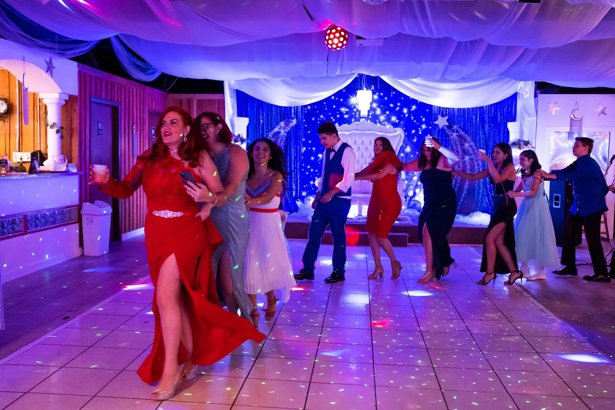 People dancing and celebrating at a party with colorful lighting and a decorated backdrop featuring stars and moon shapes.
