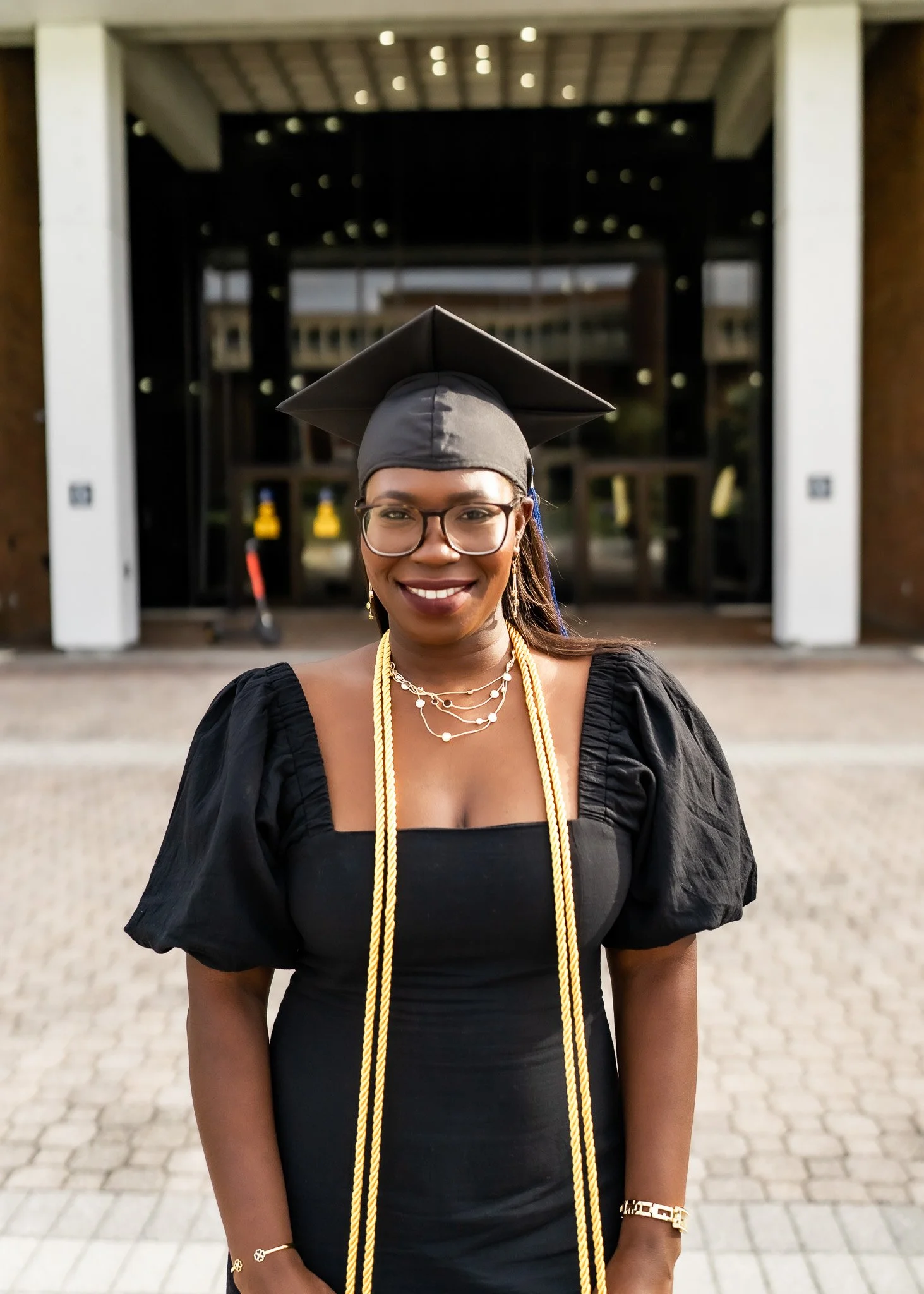 A young woman in graduation cap and gown smiling outside a building.