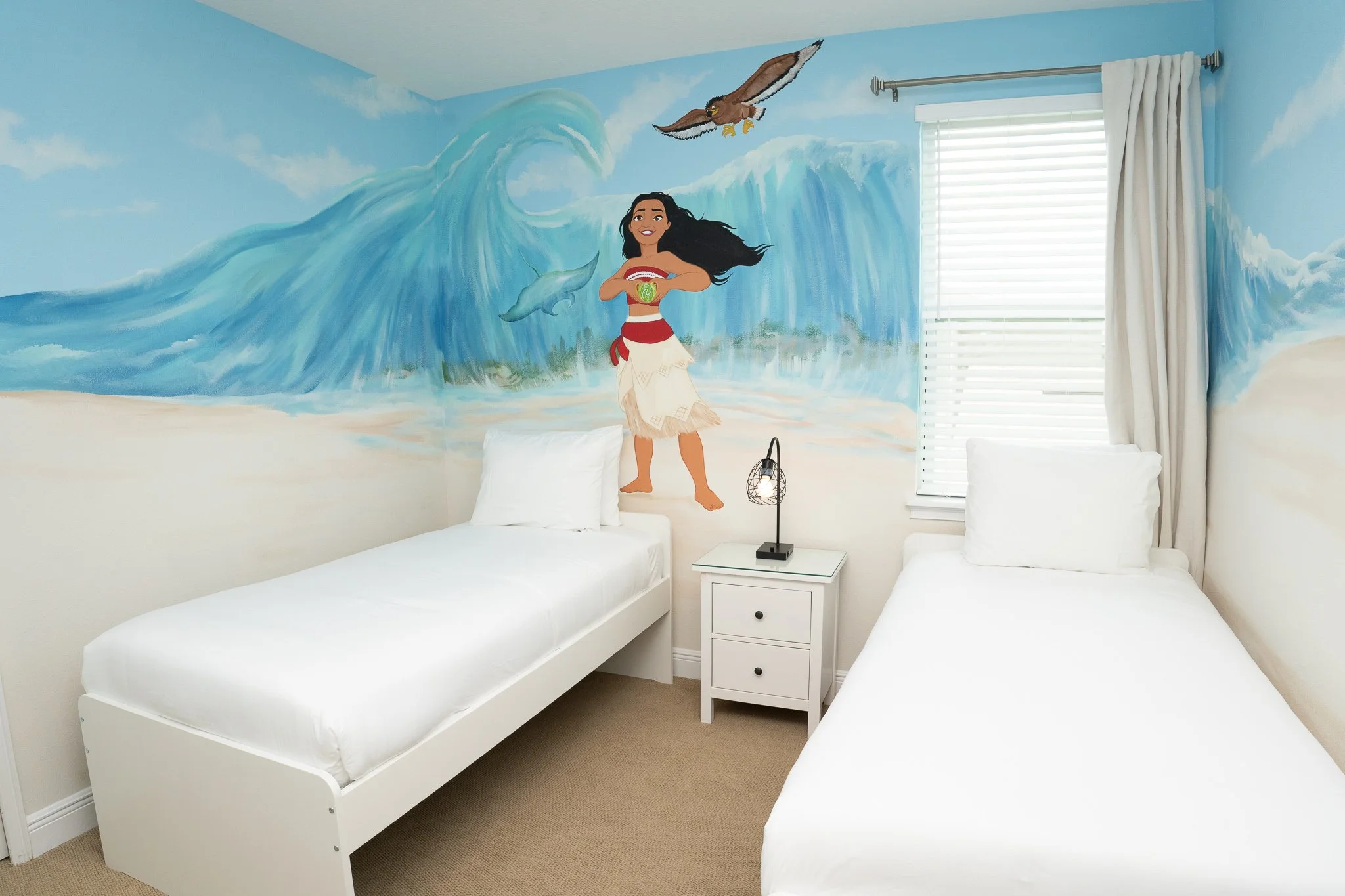 Twin beds with white bedding in a beach-themed mural room, featuring a girl in traditional attire, an eagle, and dolphins painted on the wall.