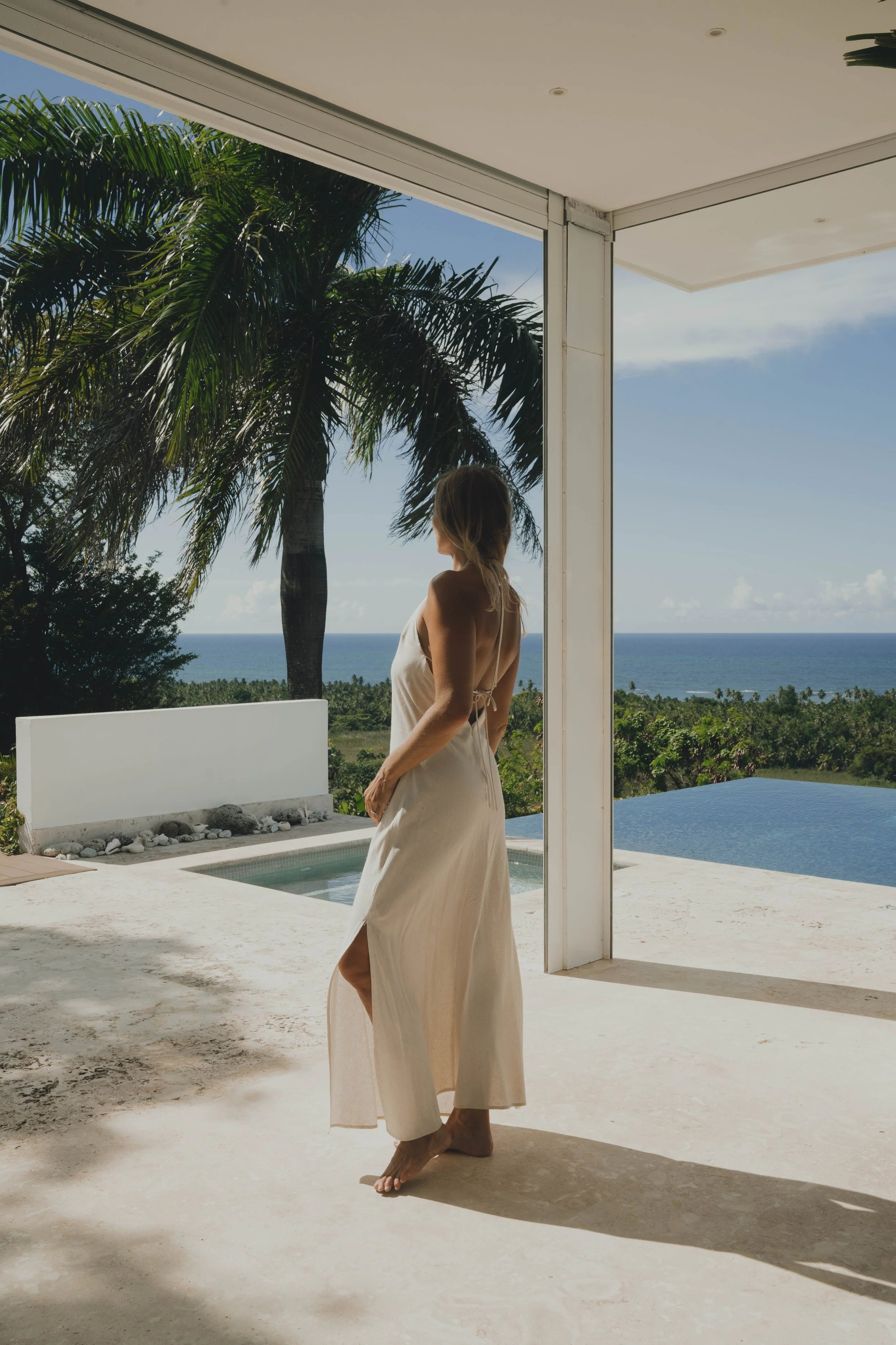 Lifestyle model standing in a luxury beachfront villa, natural resort and travel lifestyle scene with palm trees and ocean.
