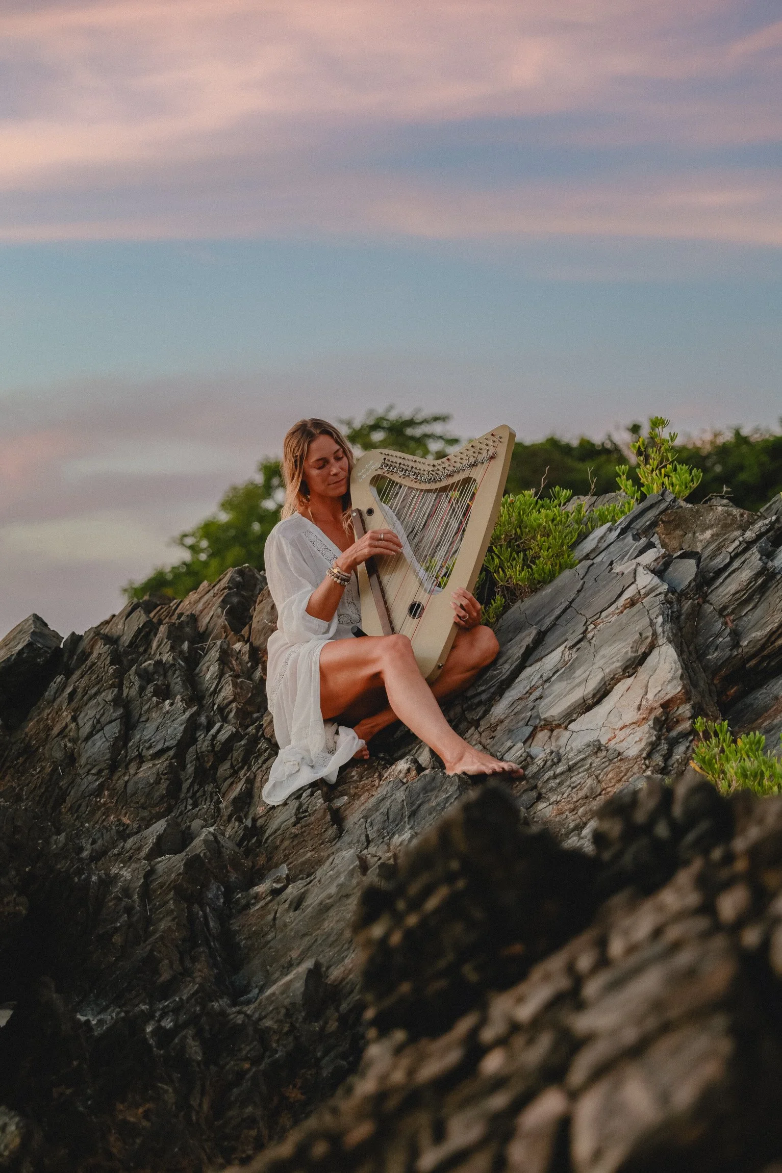 Coastal lifestyle portrait of a harpist performing on seaside rocks.