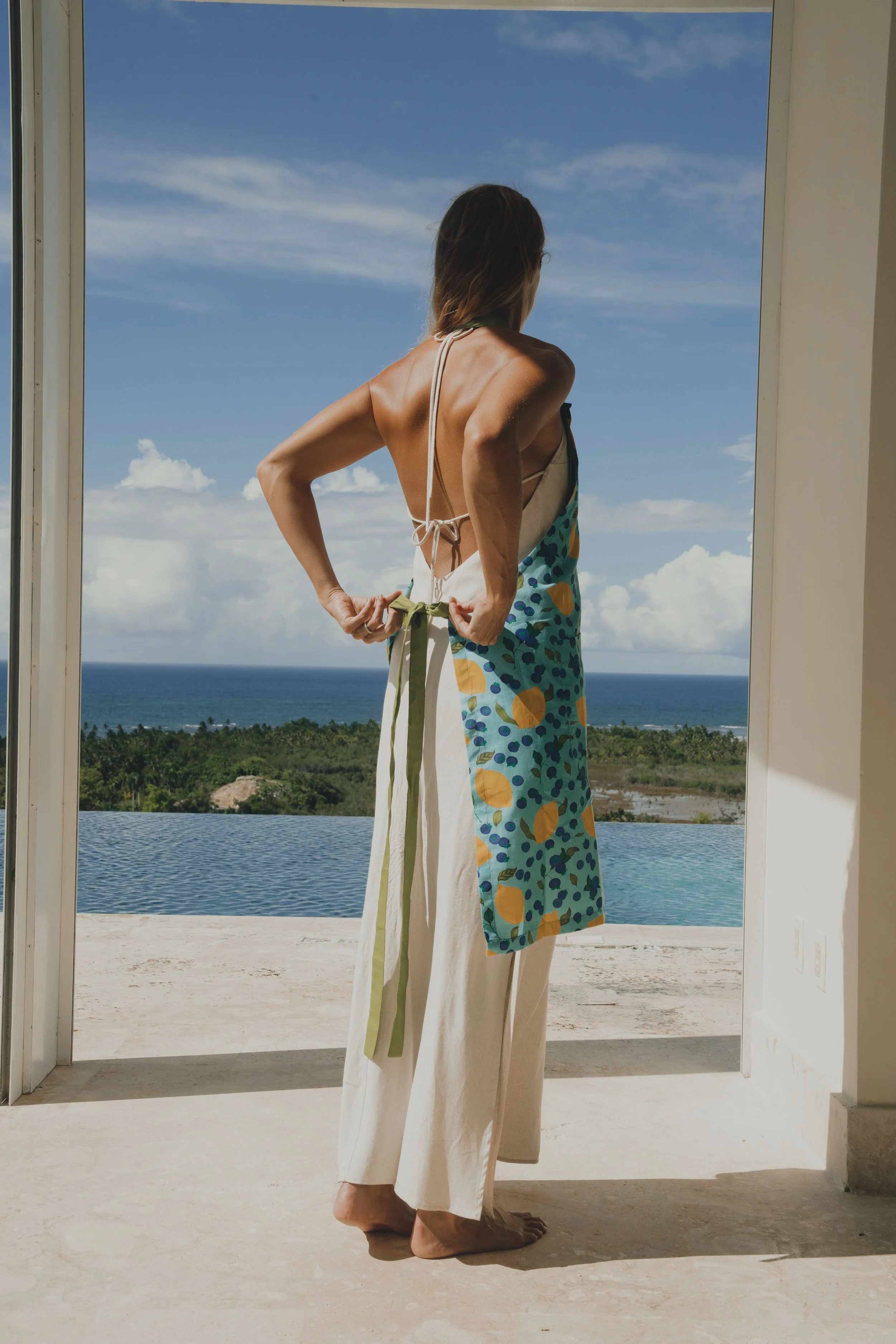 Lifestyle model tying an apron in a sunlit tropical villa kitchen, capturing relaxed coastal living and resort lifestyle imagery.