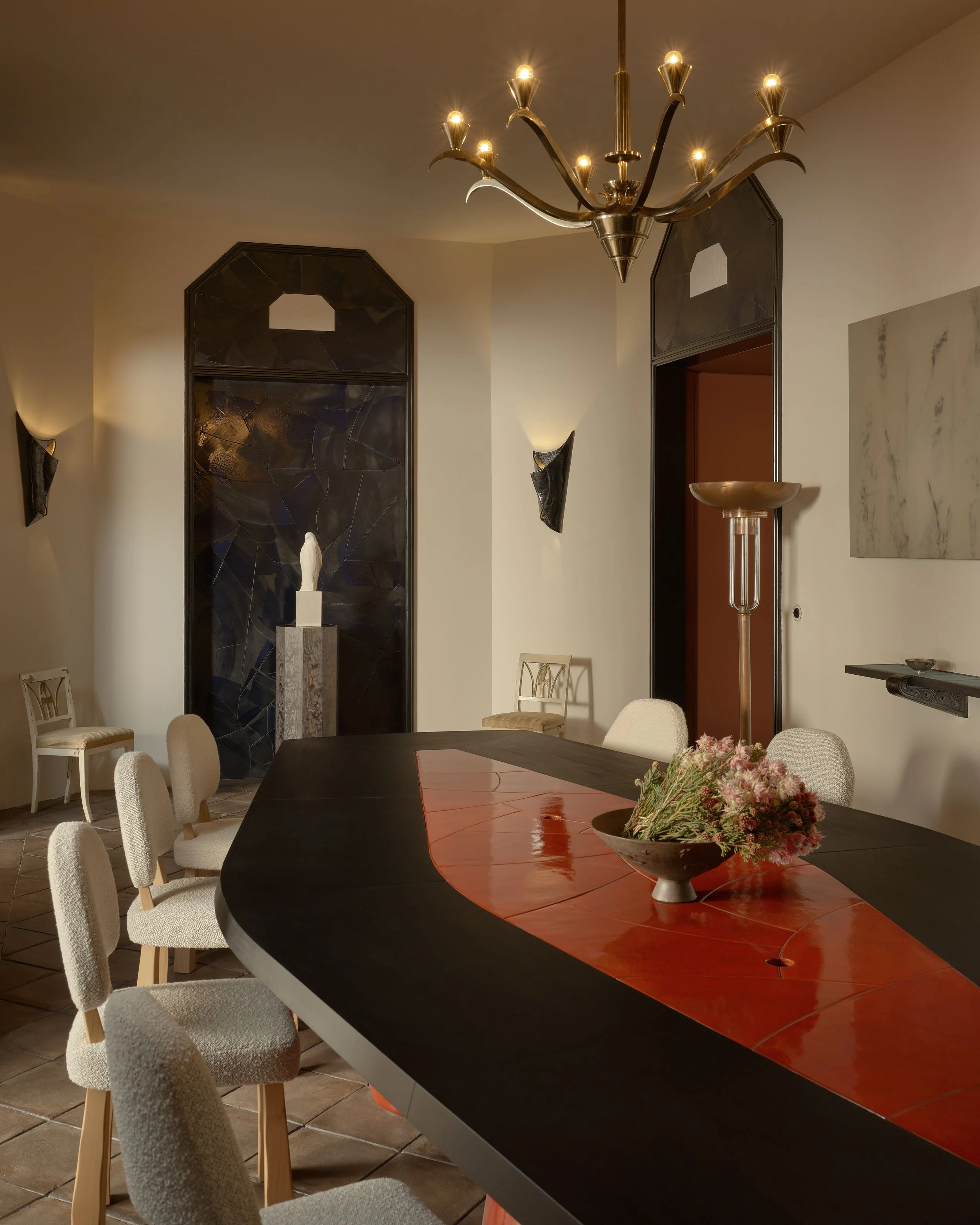 Elegant dining room with a large oval table, white upholstered chairs, a chandelier, decorative wall sconces, and a sculpture on a pedestal.