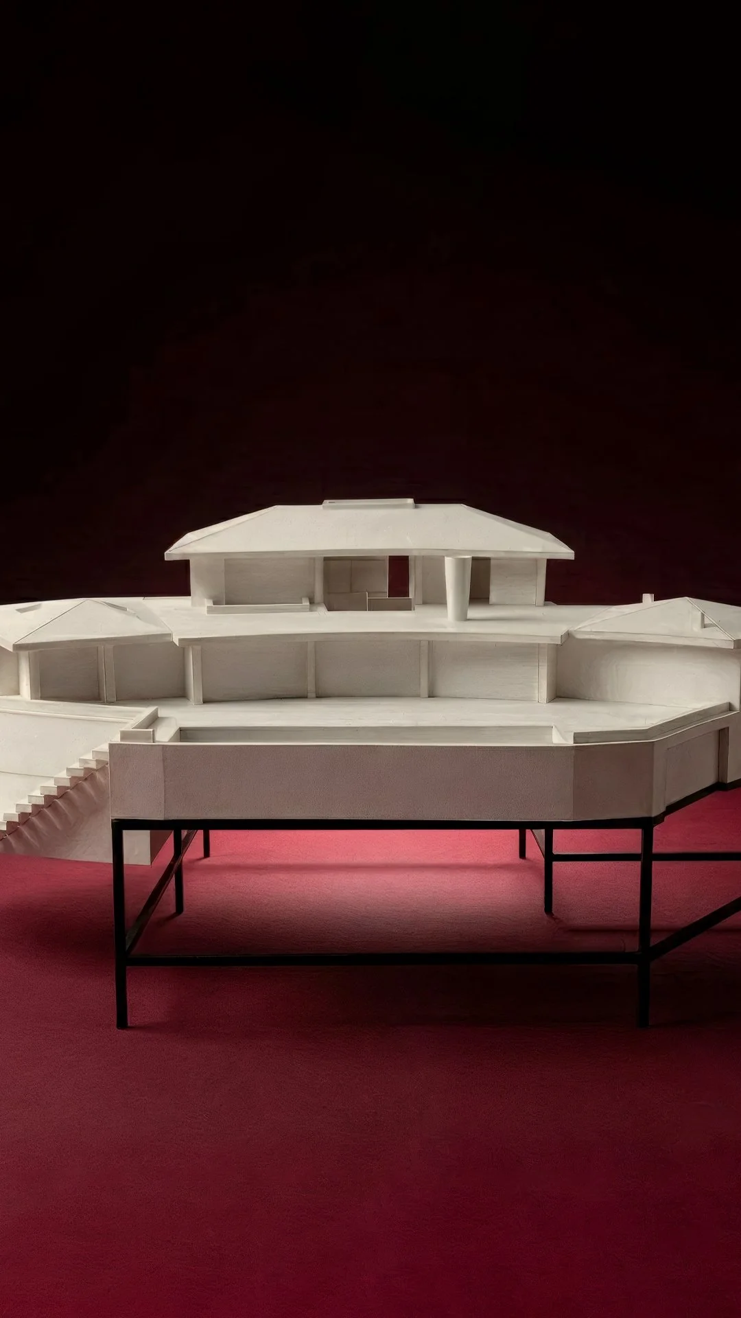 White scale model of a house on a steel stand, against deep red