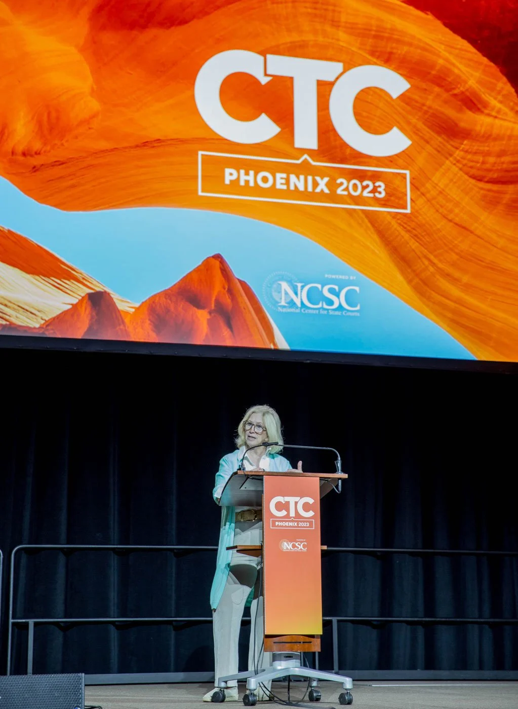 The keynote speaker at a branded podium, in front of a branded slide.