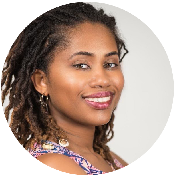 A woman with shoulder length locs wearing a patterned top smiling in front of a neutral background