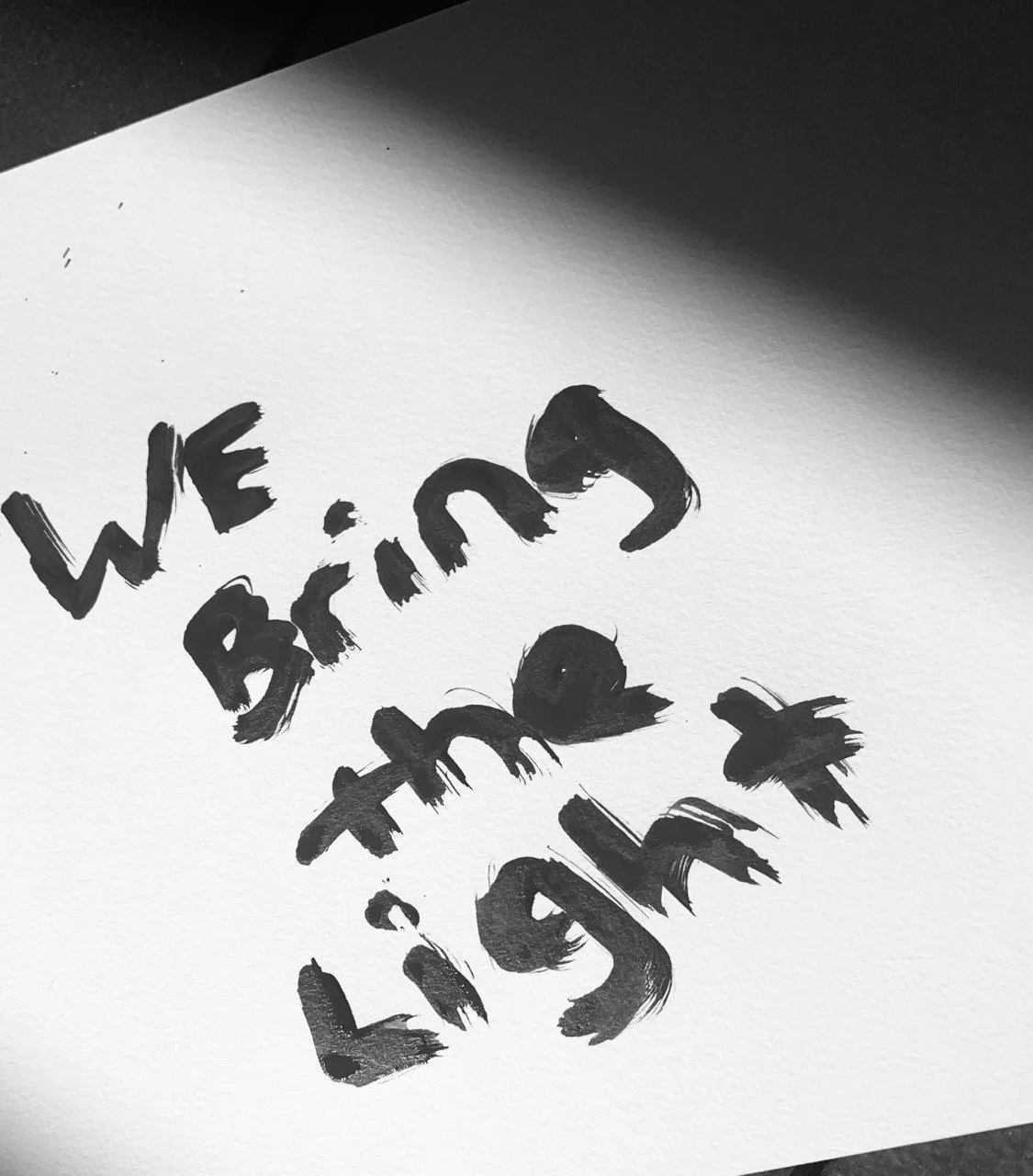 A black and white image of painting on canvas that read: We bring the light.