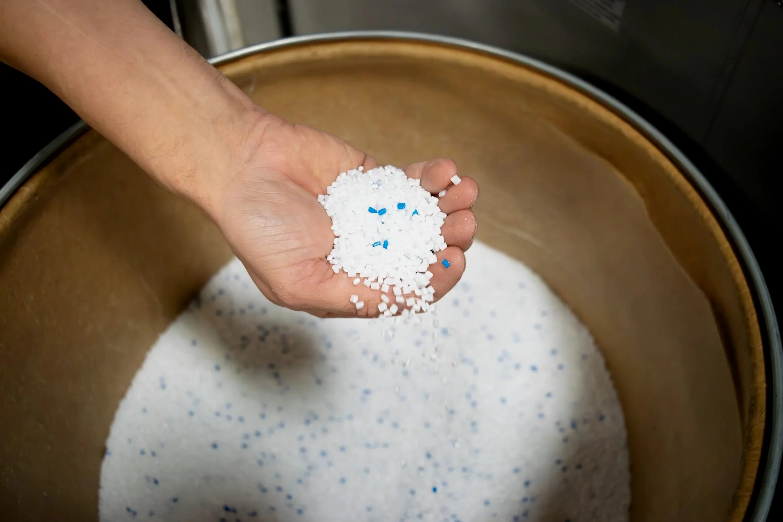 An employee hand holds a handful of material used for Injection Molding. It is white with specs of blue to accurately match the color the customer requests.