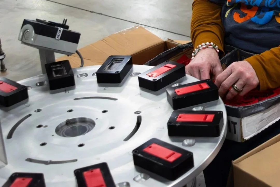 A second view of a Fey Industries team member loads the sonic welding machine with a bright red product and safely completes the job.