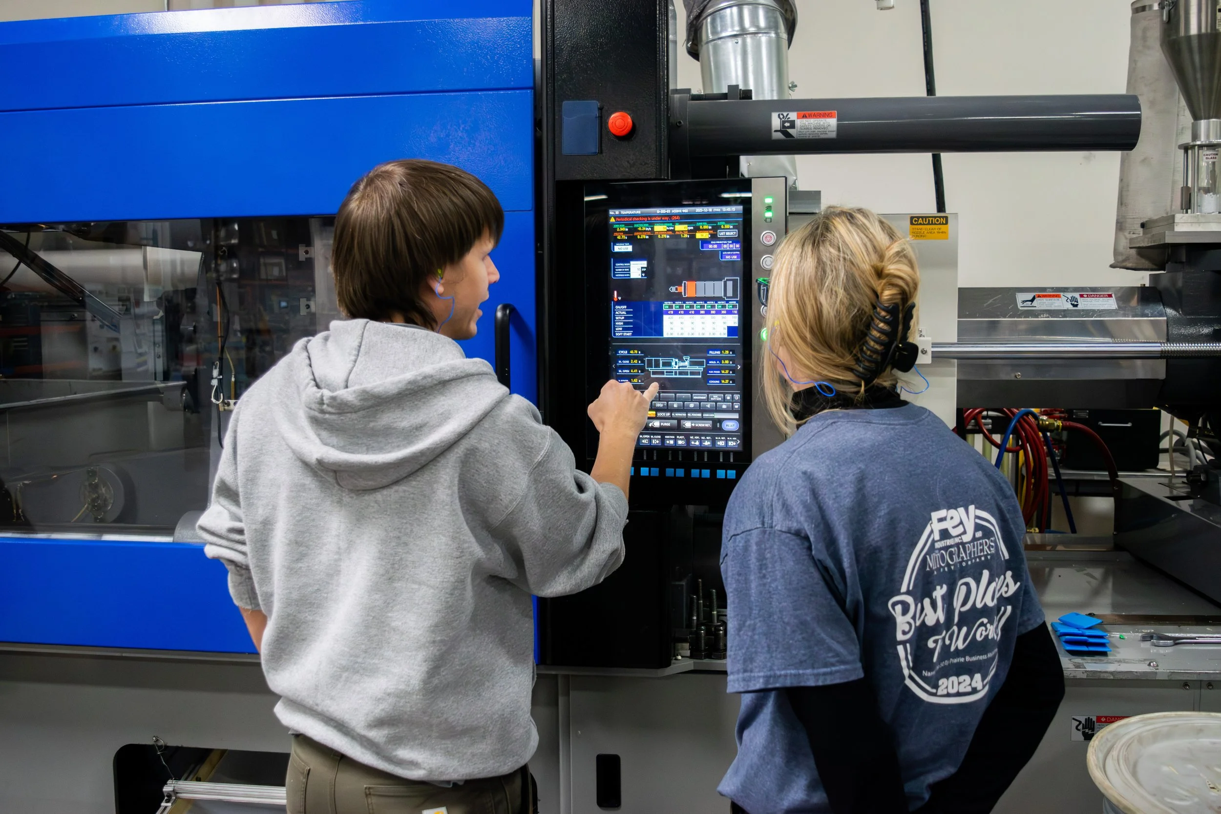 Two Fey Industries employees work together on setting a high end machine up to create a bright blue product for a customer.