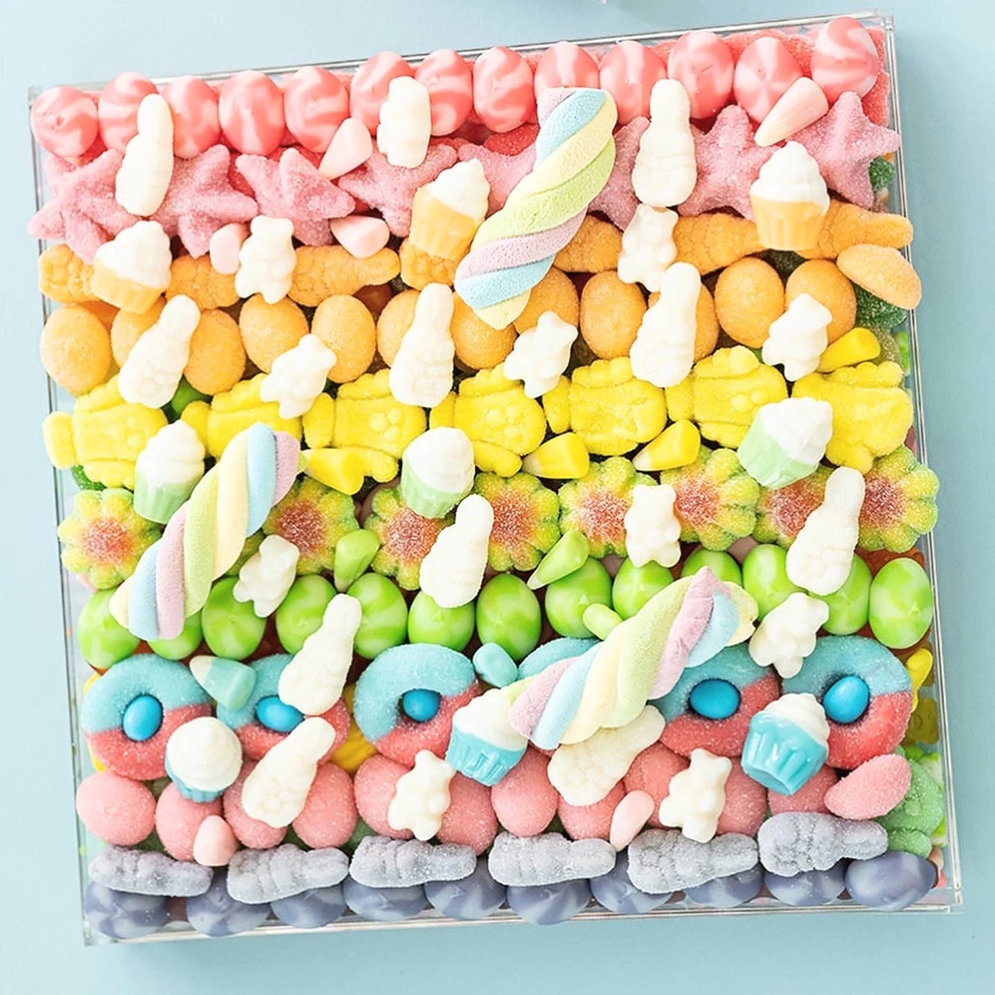 Assorted colorful candies on a square glass tray on a pink background.