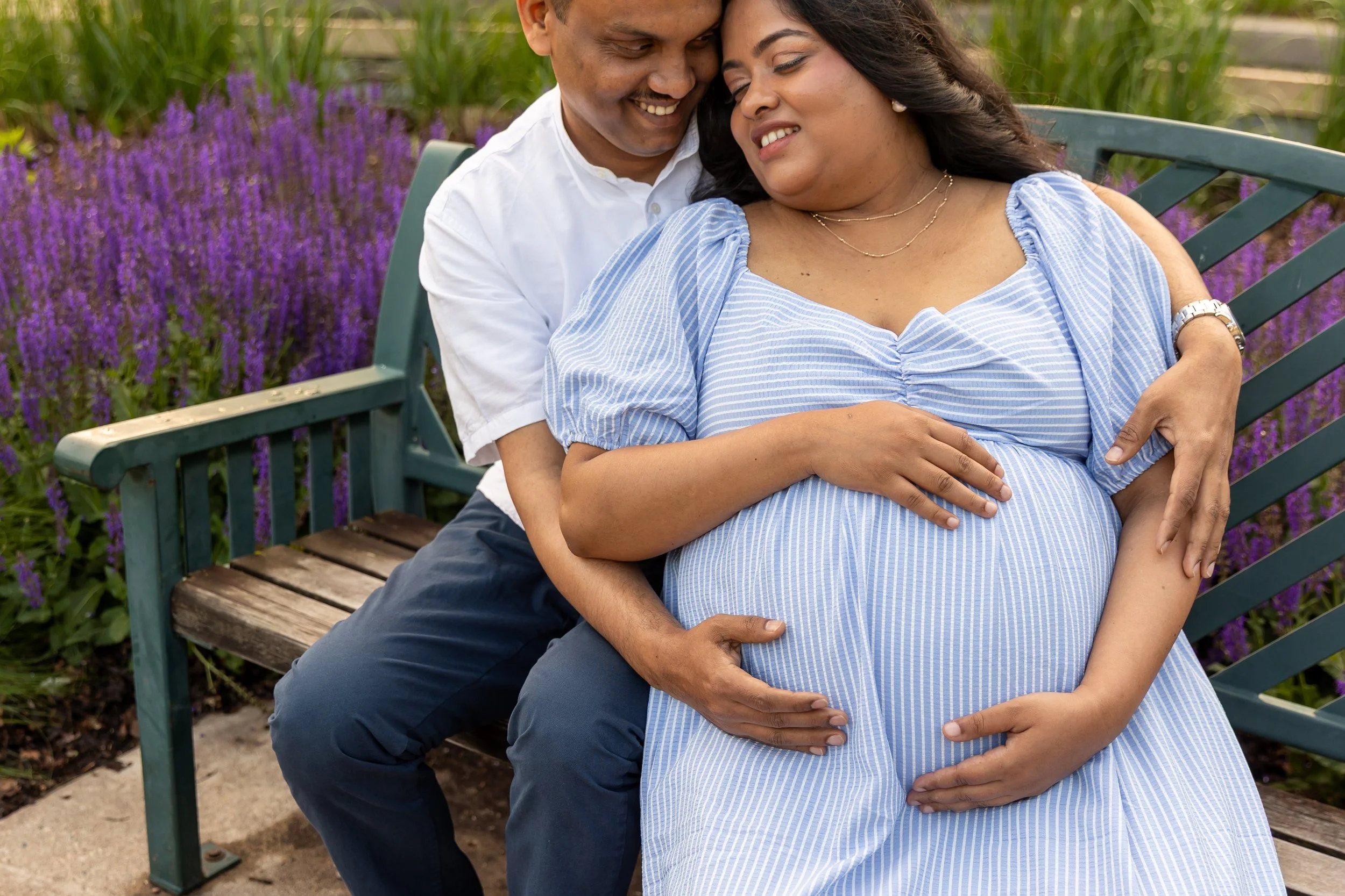 Soon to be-Father and mother embrace each other in a Minneapolis park while embracing the baby bump.