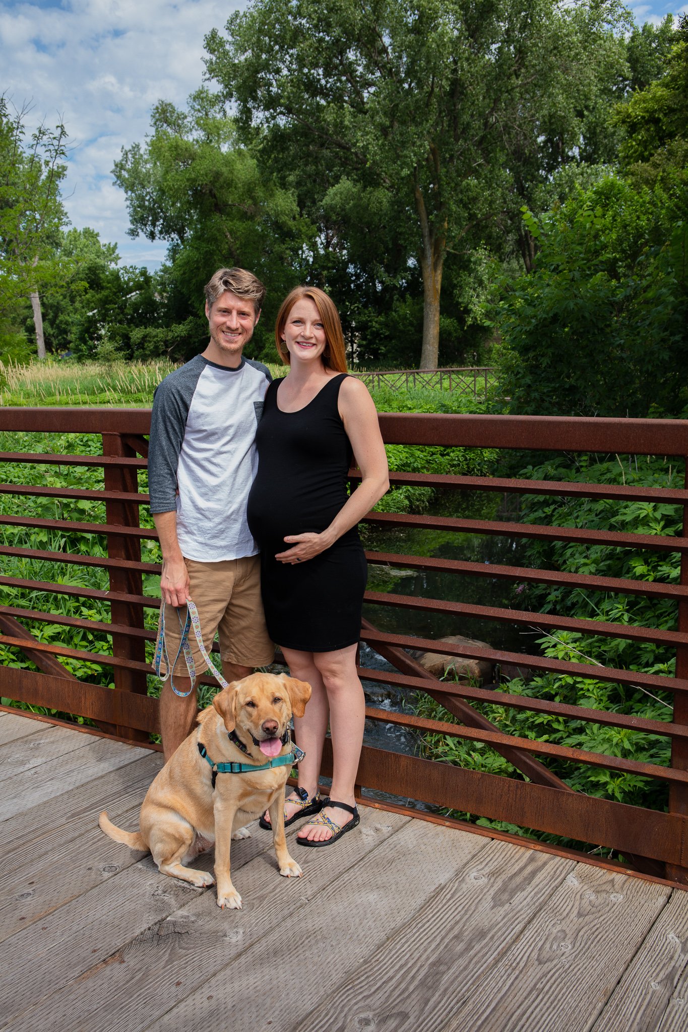 Maternity session, mother holding baby bump while standing with father and dog