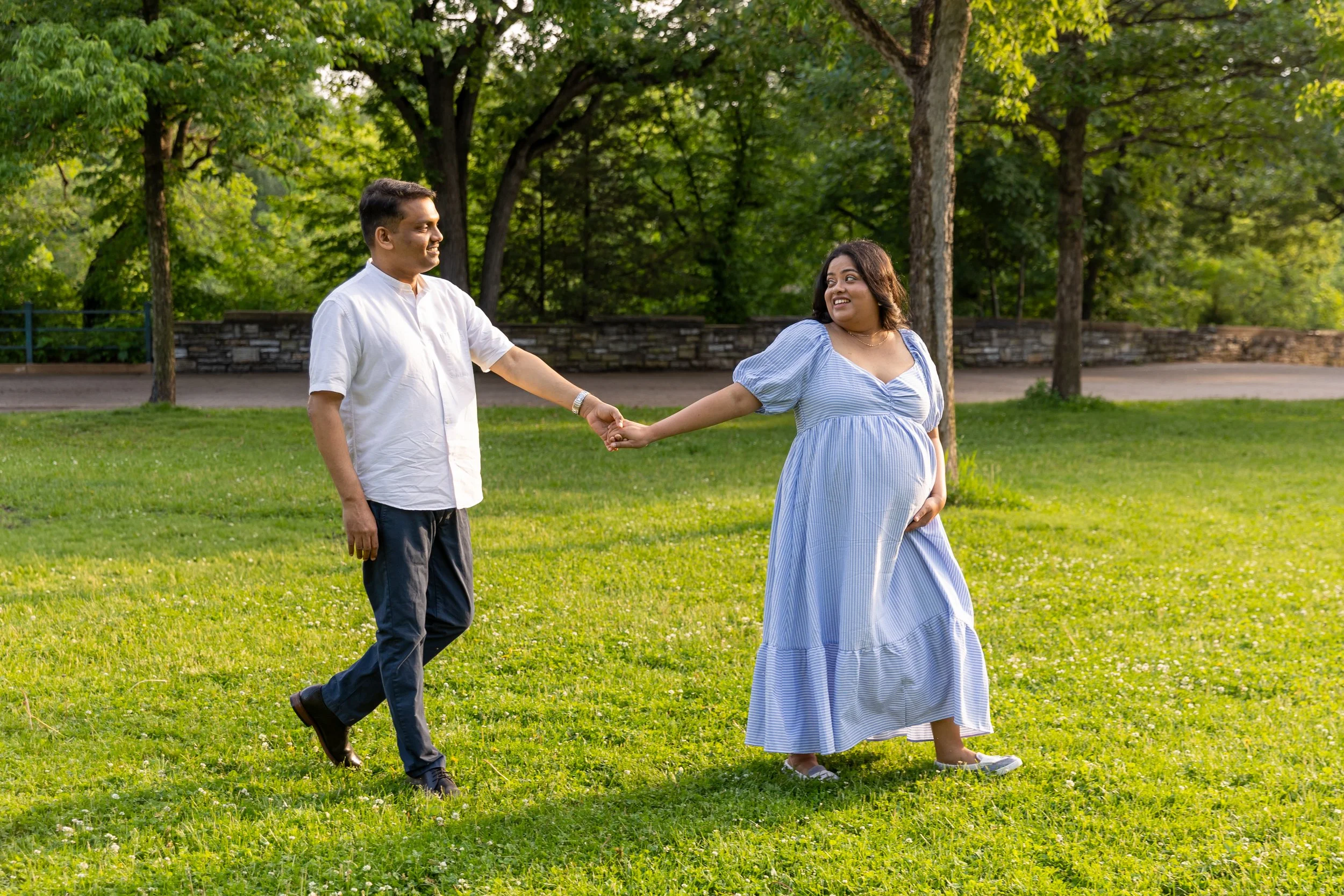 Maternity session - A mother is holding hands with the father leading the way walking in Minnehaha Falls Park holding hands smiling at each other